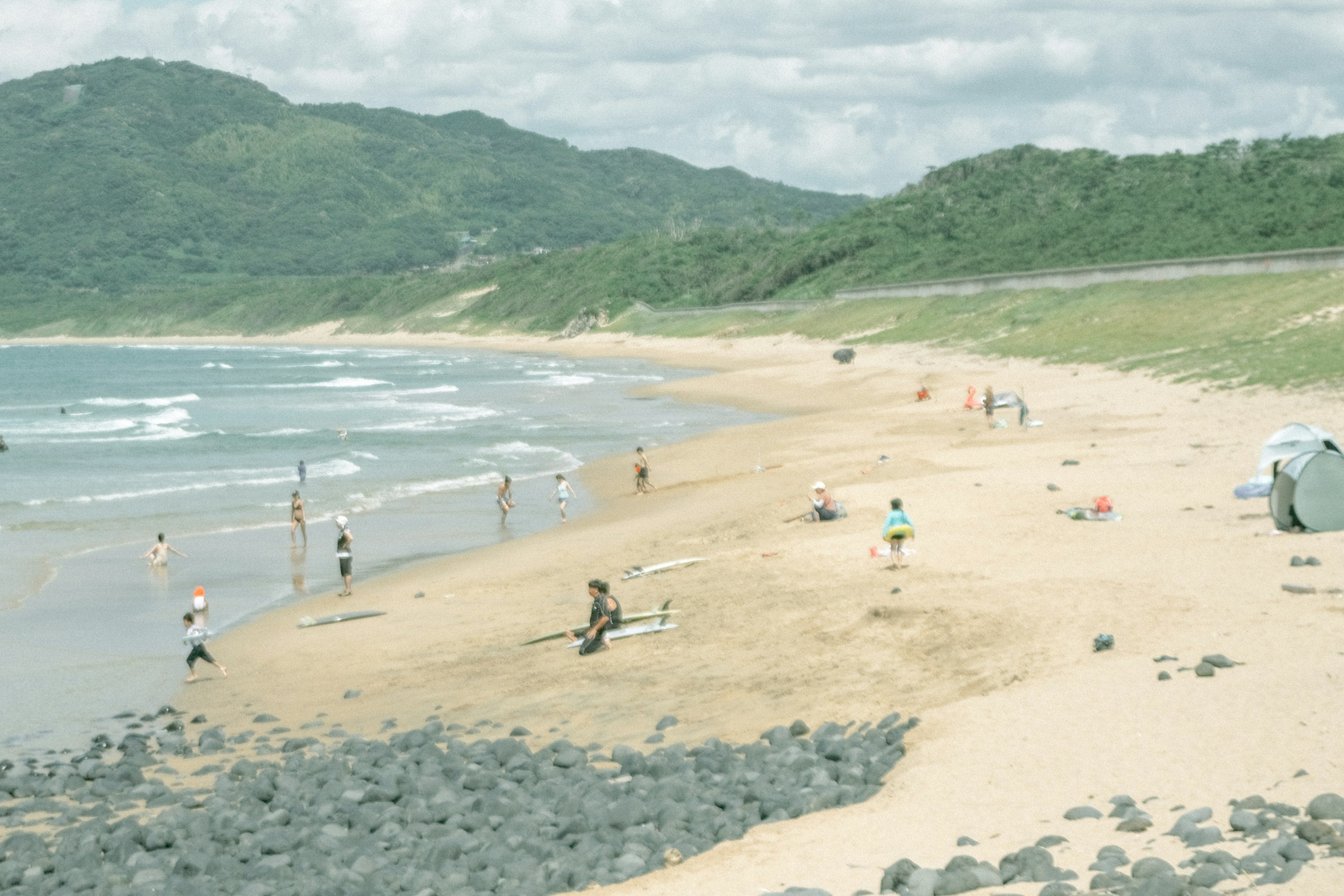 人々がビーチで楽しんでいる風景 緑の山々と波がある海