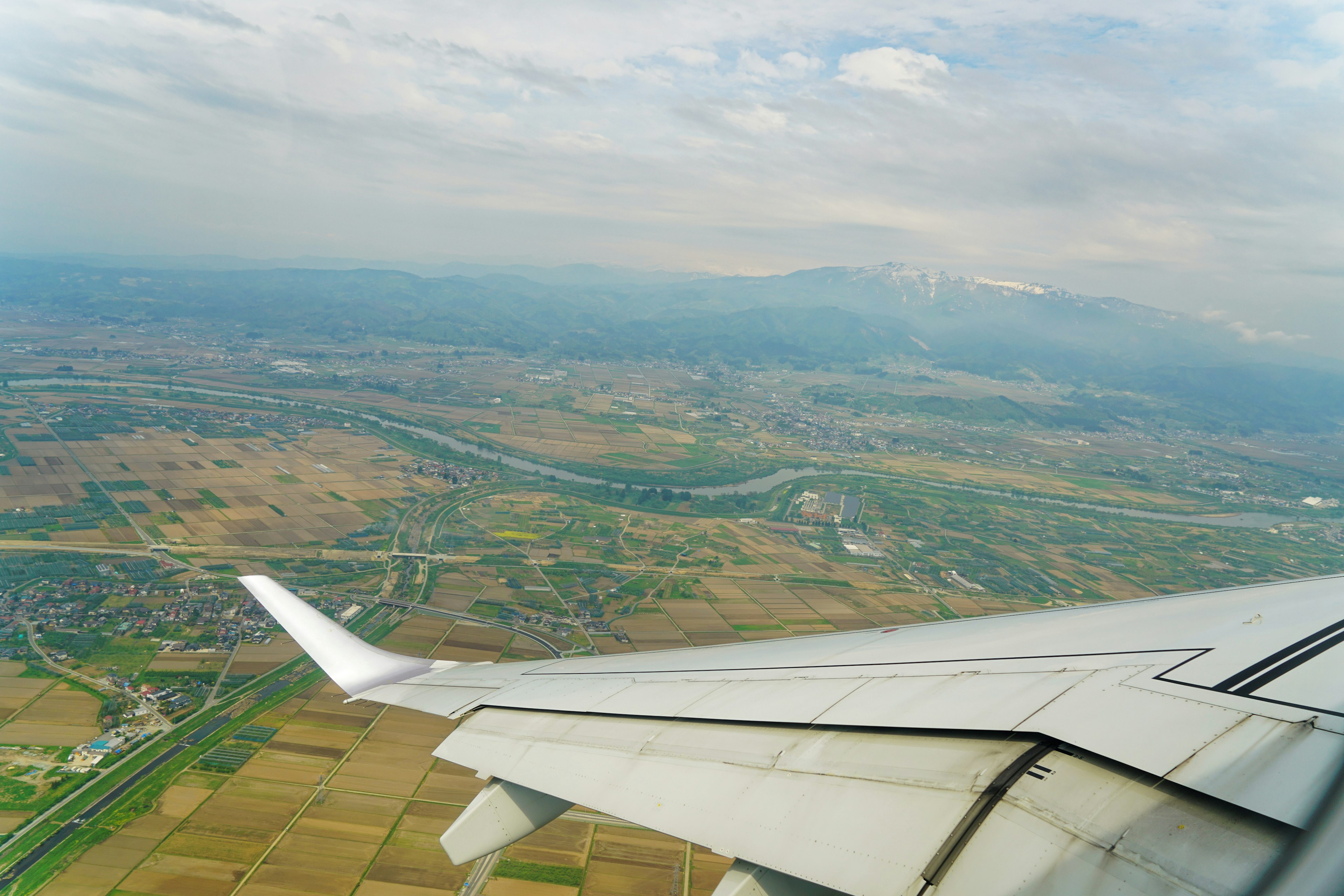 Luftaufnahme mit einem Flugzeugflügel und einer weitläufigen Landschaft