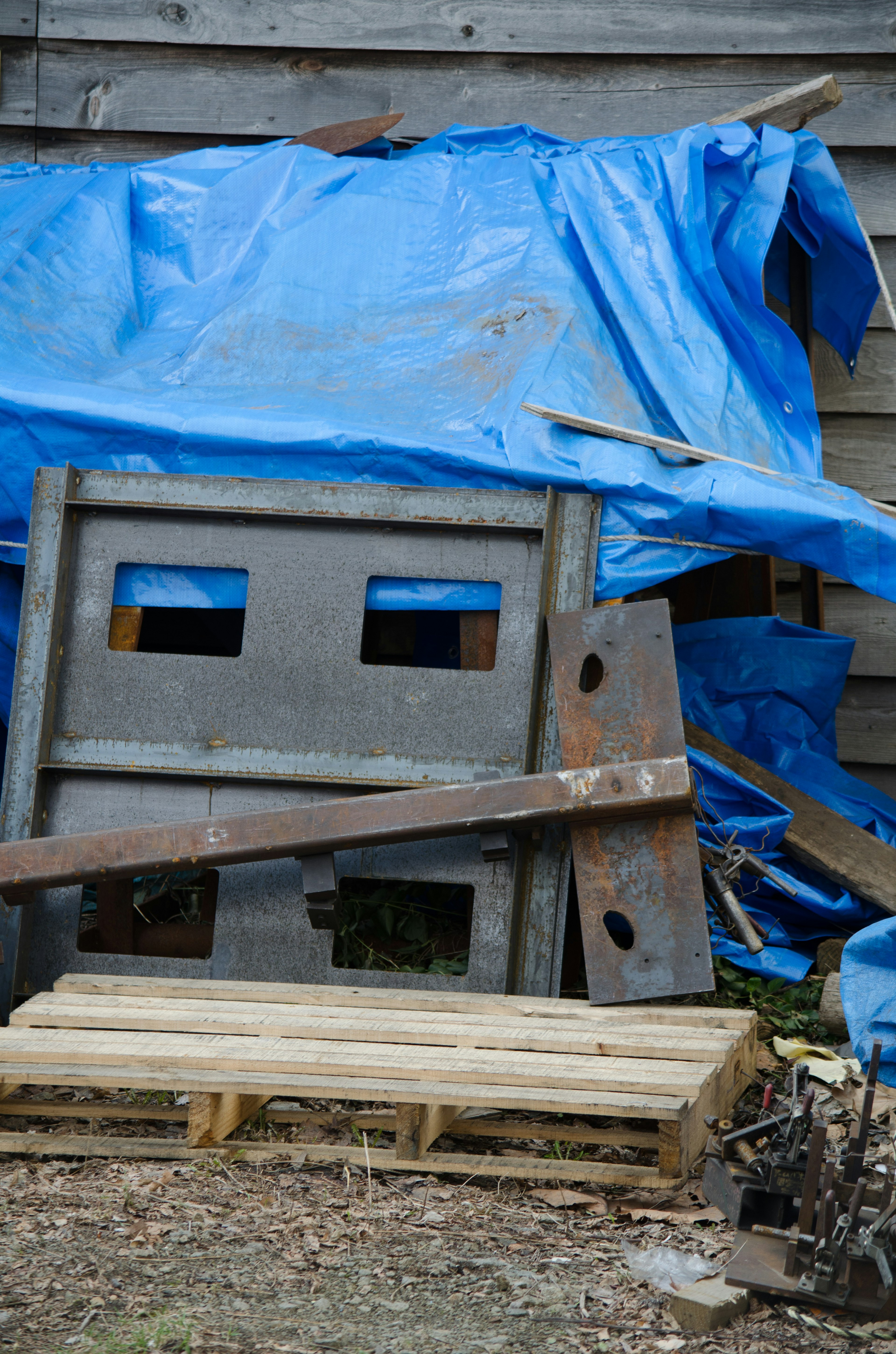 A scene of stacked wooden pallets and metal debris covered with a blue tarp