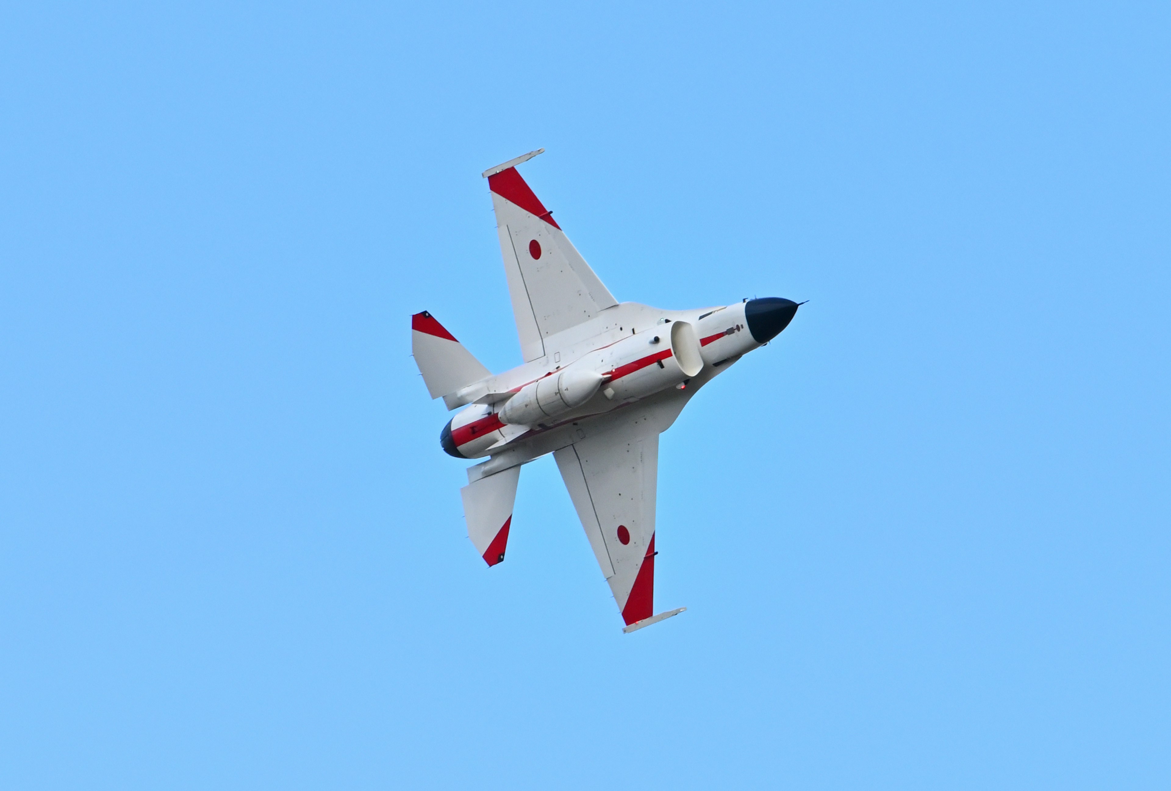 Red and white Japanese fighter jet flying against a blue sky