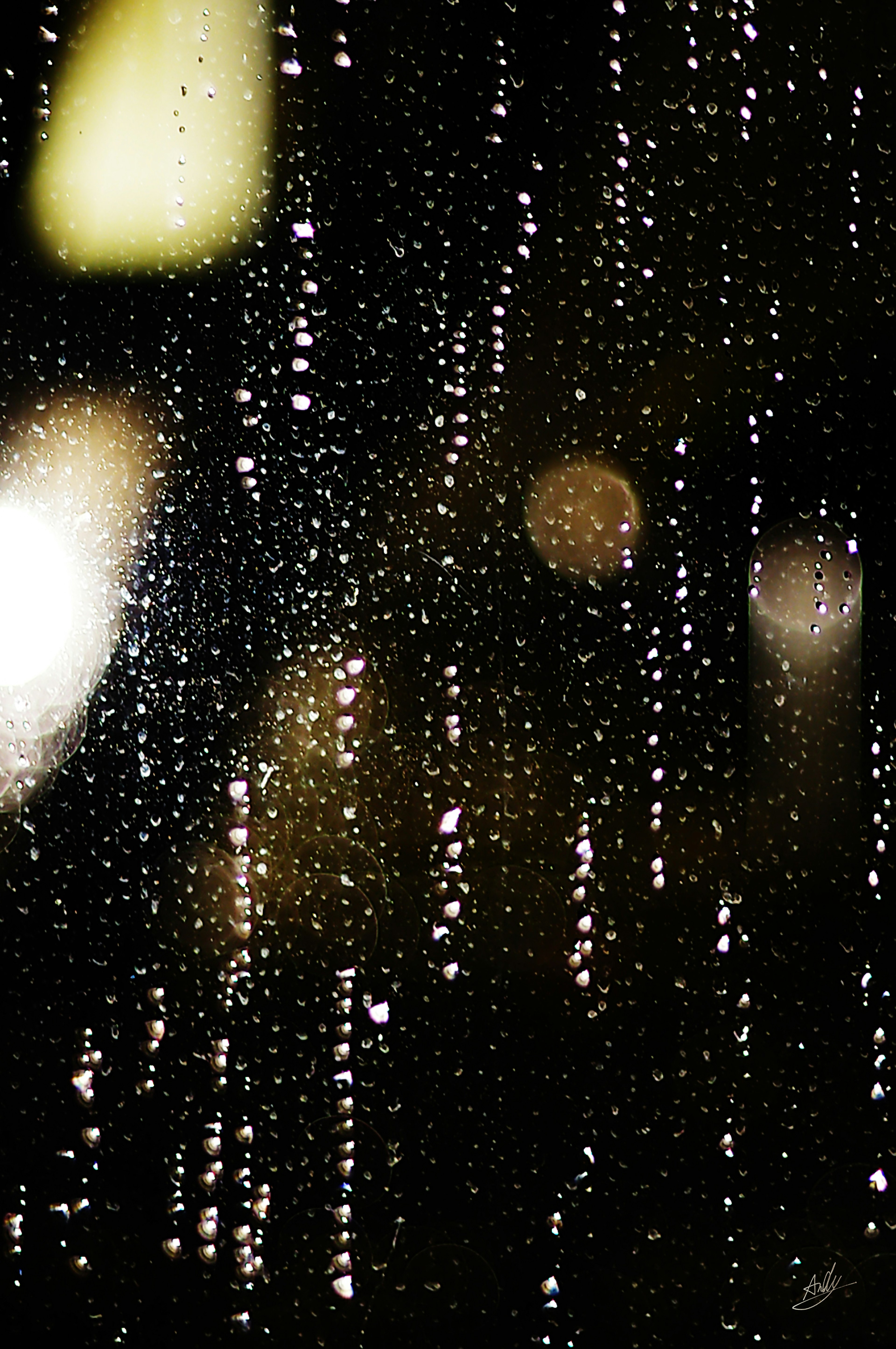 Gotas de lluvia cayendo por una ventana con luces de la ciudad borrosas