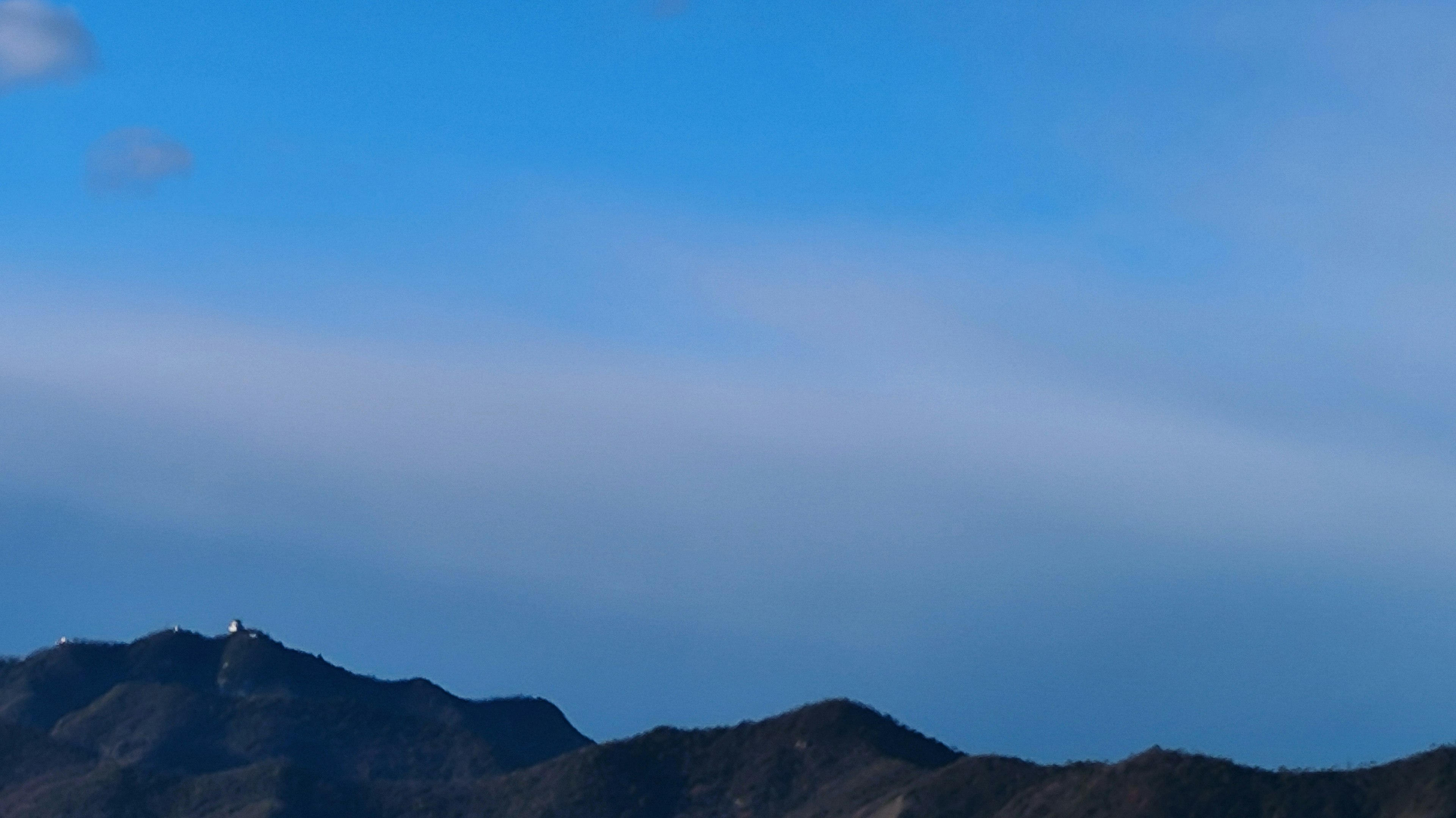 青い空と山々の風景で遠くの山頂に白い点が見える