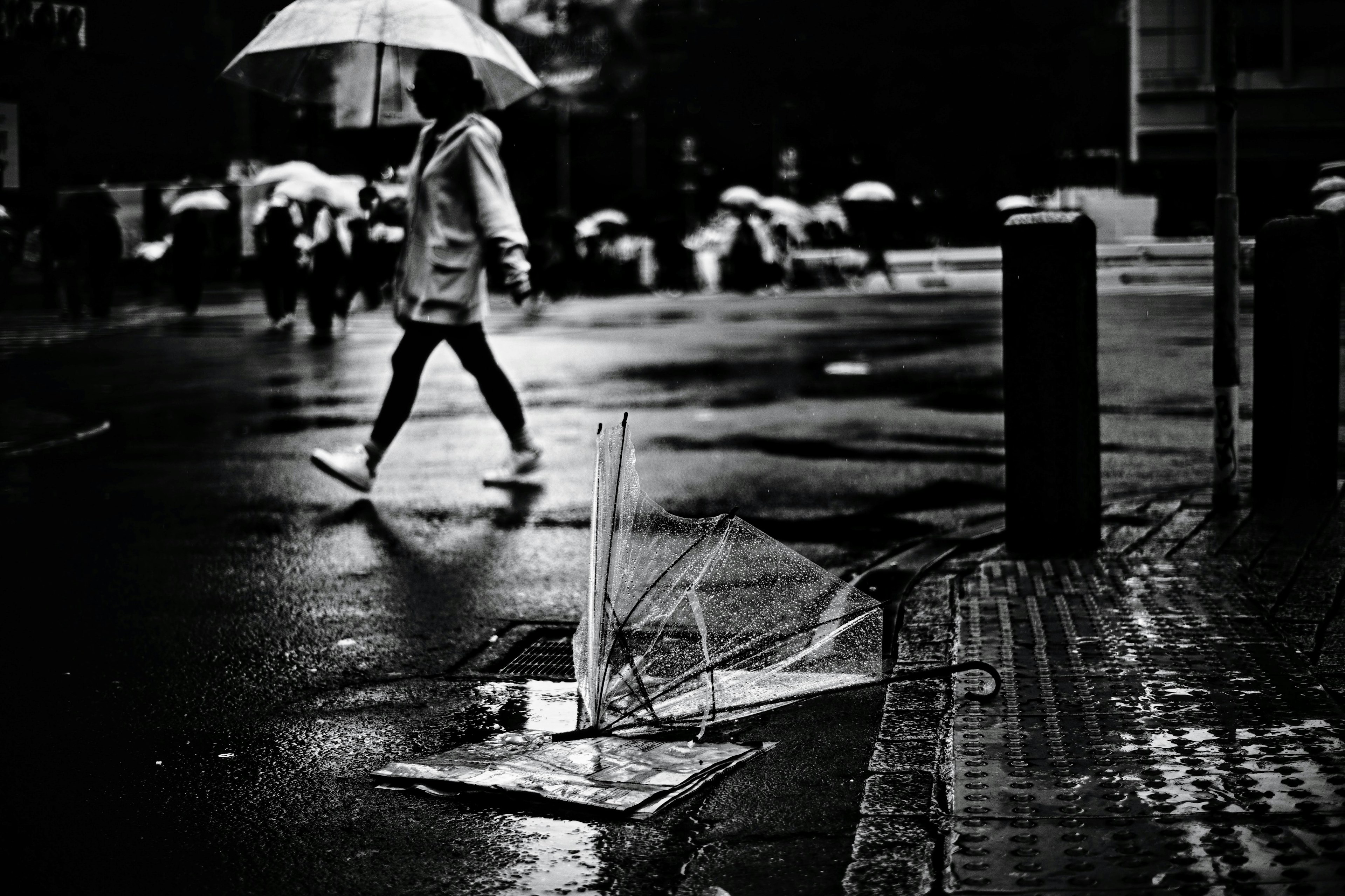 Image en monochrome d'une personne marchant sous la pluie avec un parapluie cassé