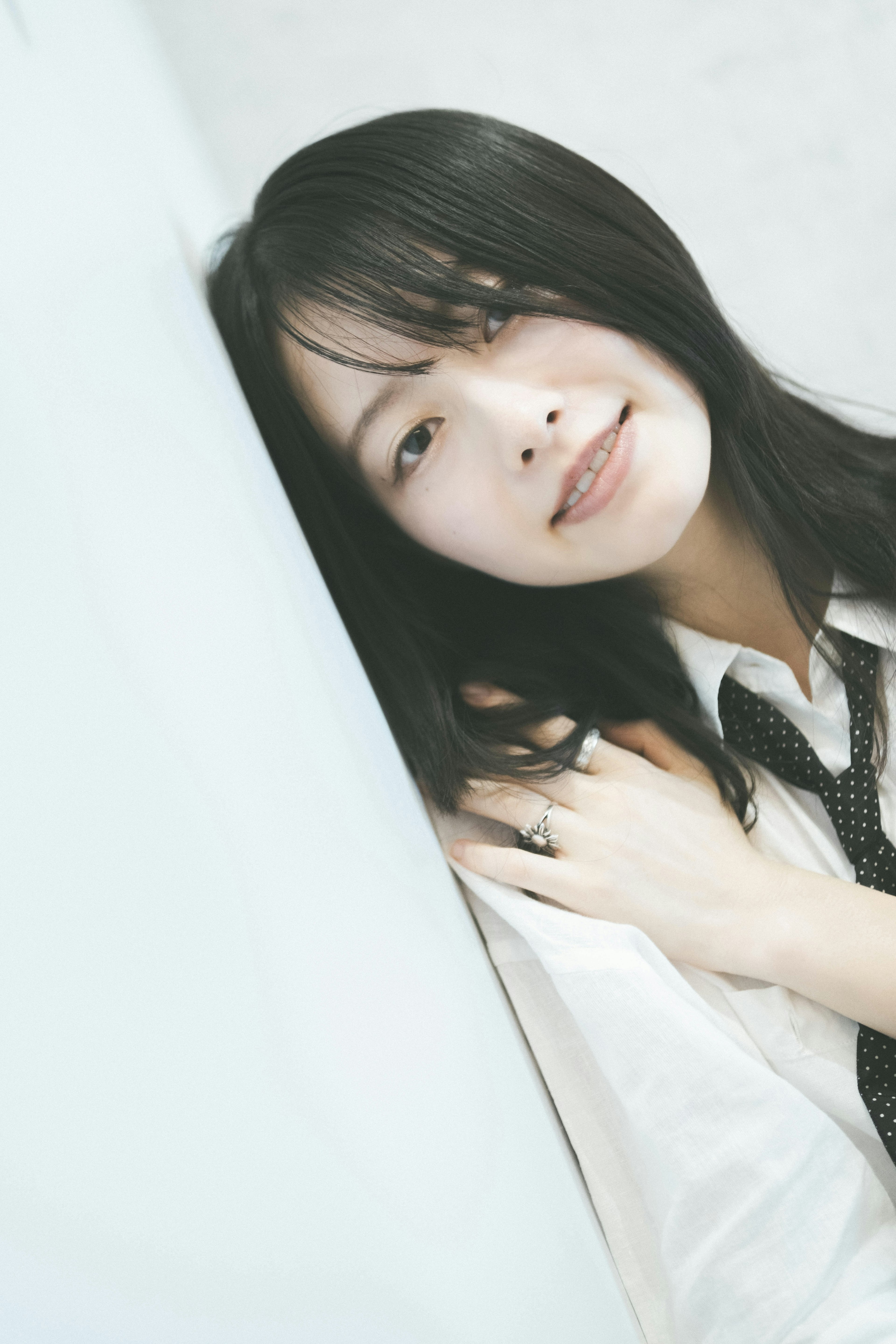 A woman in a white shirt and tie smiling while leaning against a wall