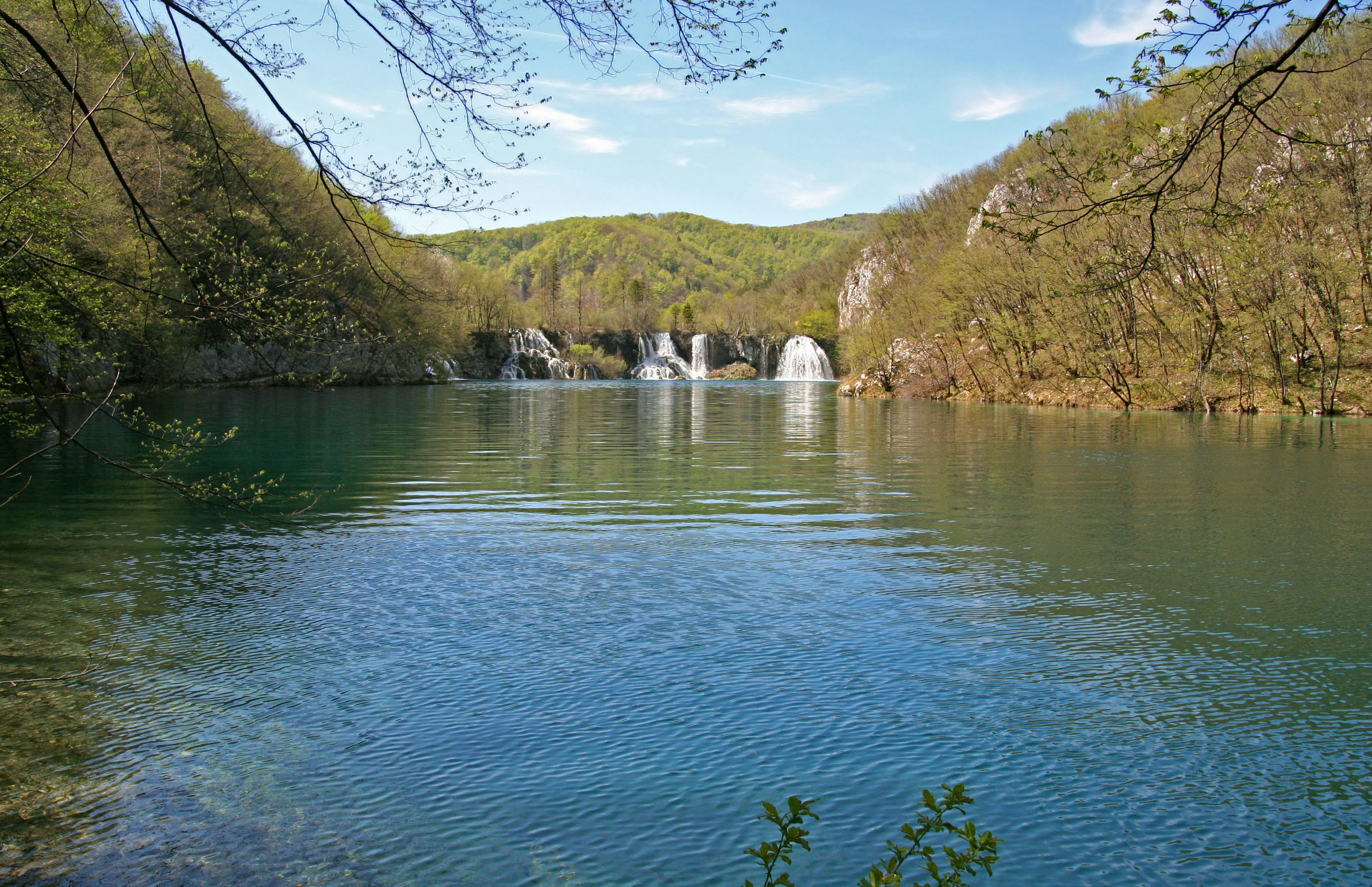 Lago sereno rodeado de vegetación exuberante con pequeñas cascadas