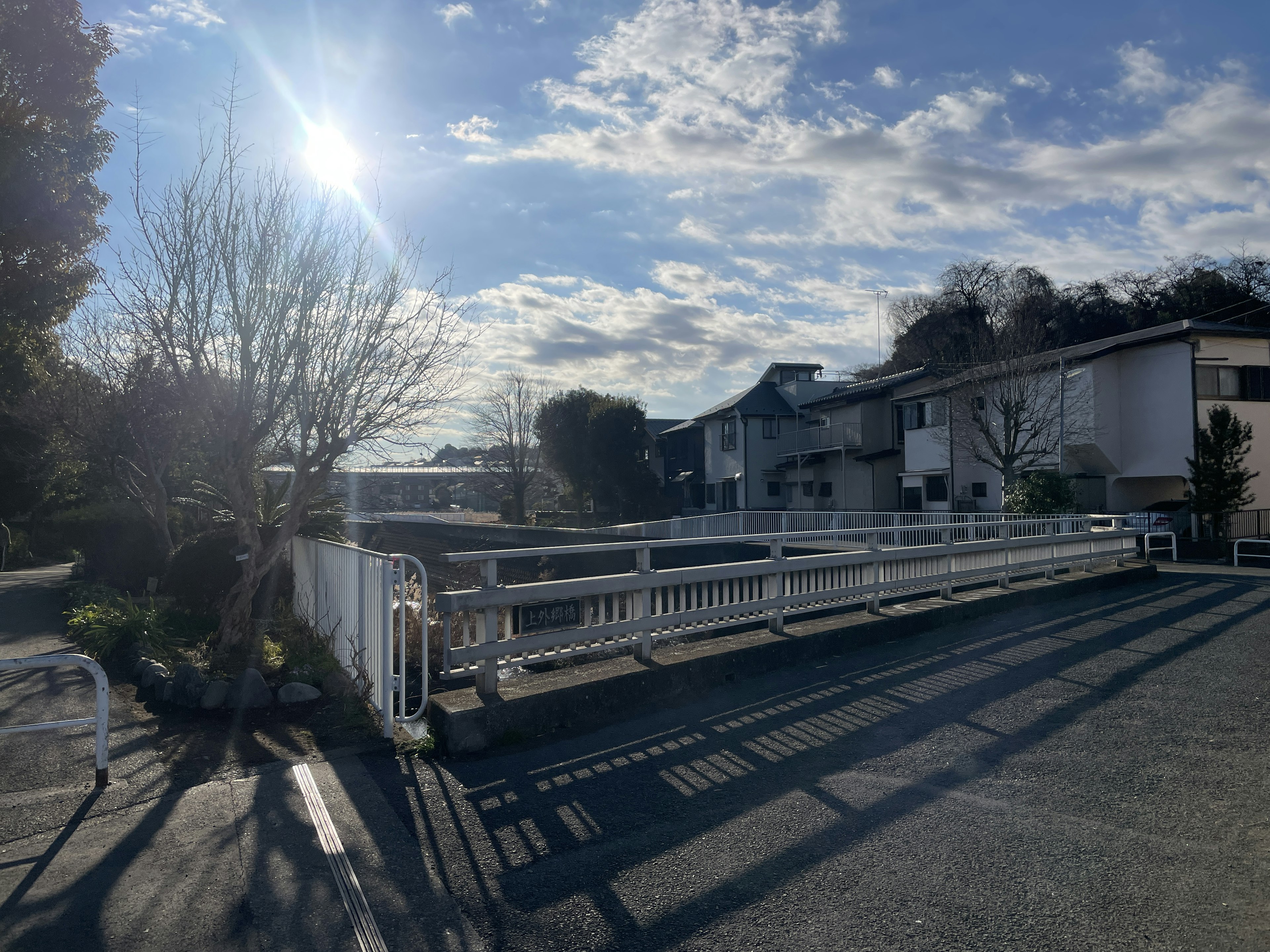 Daytime scene featuring a white guardrail and houses under a blue sky with clouds