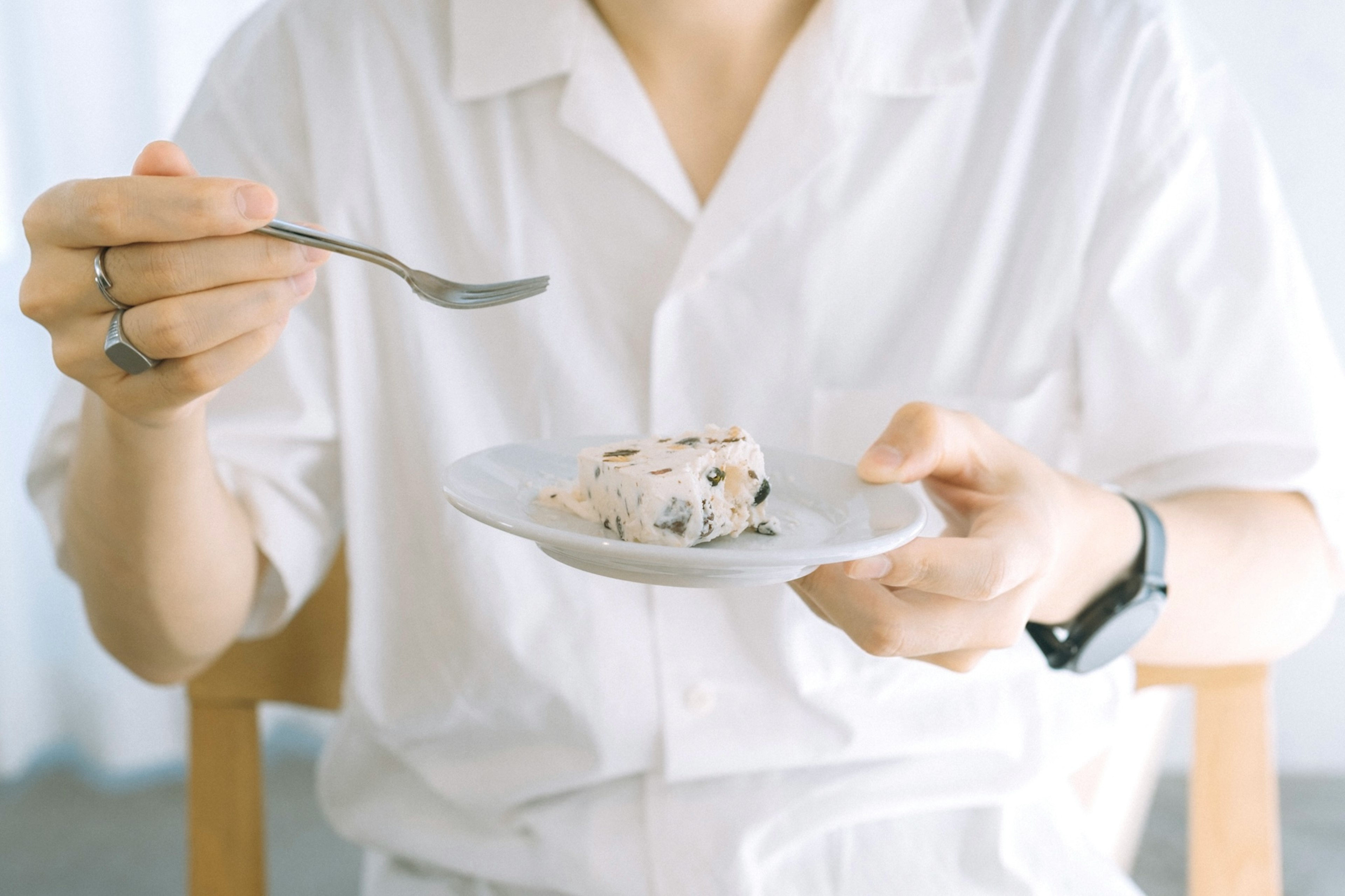 Person in a white shirt holding a plate with dessert and a fork