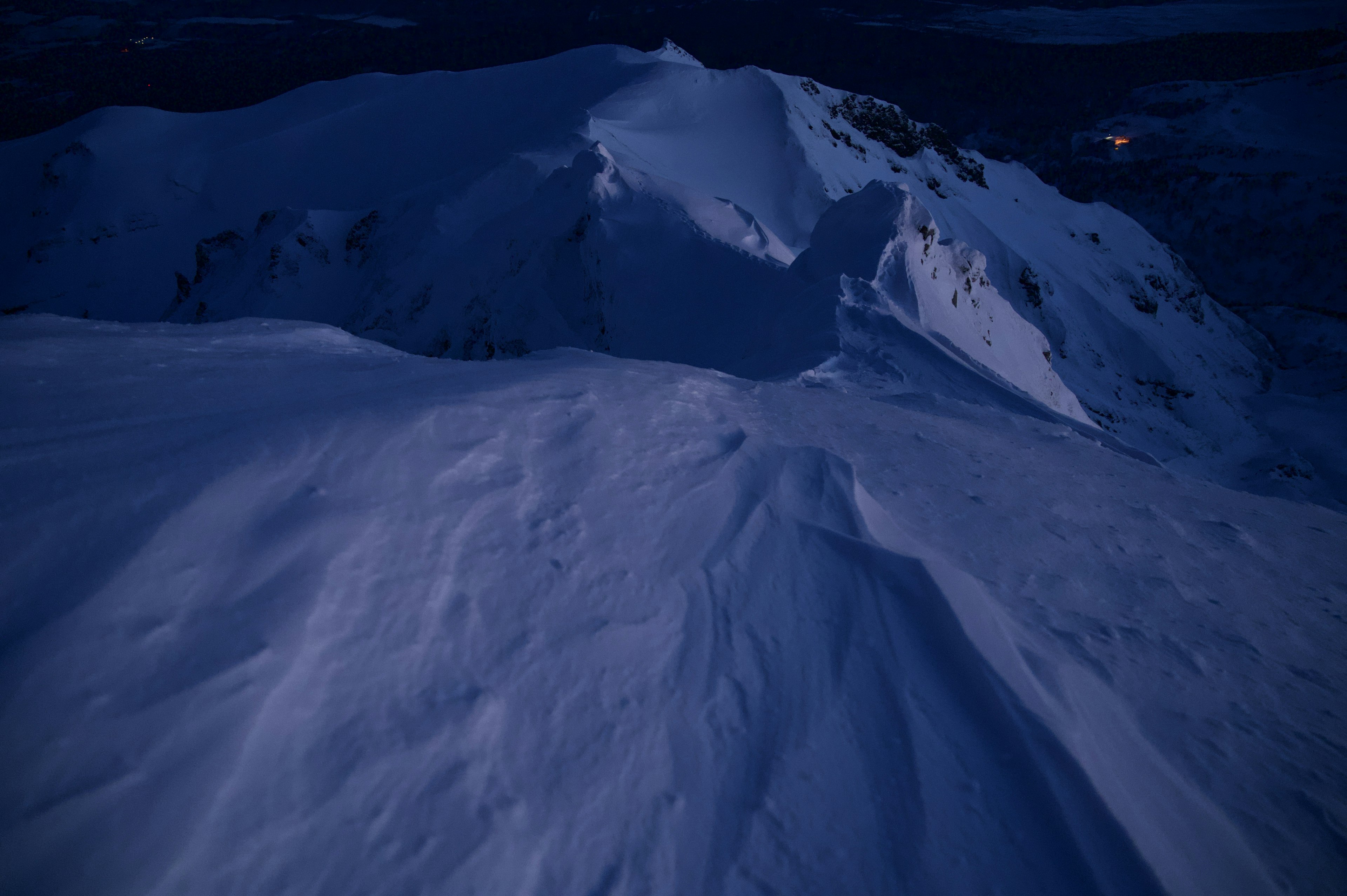 雪に覆われた山の斜面が暗闇に浮かび上がる風景