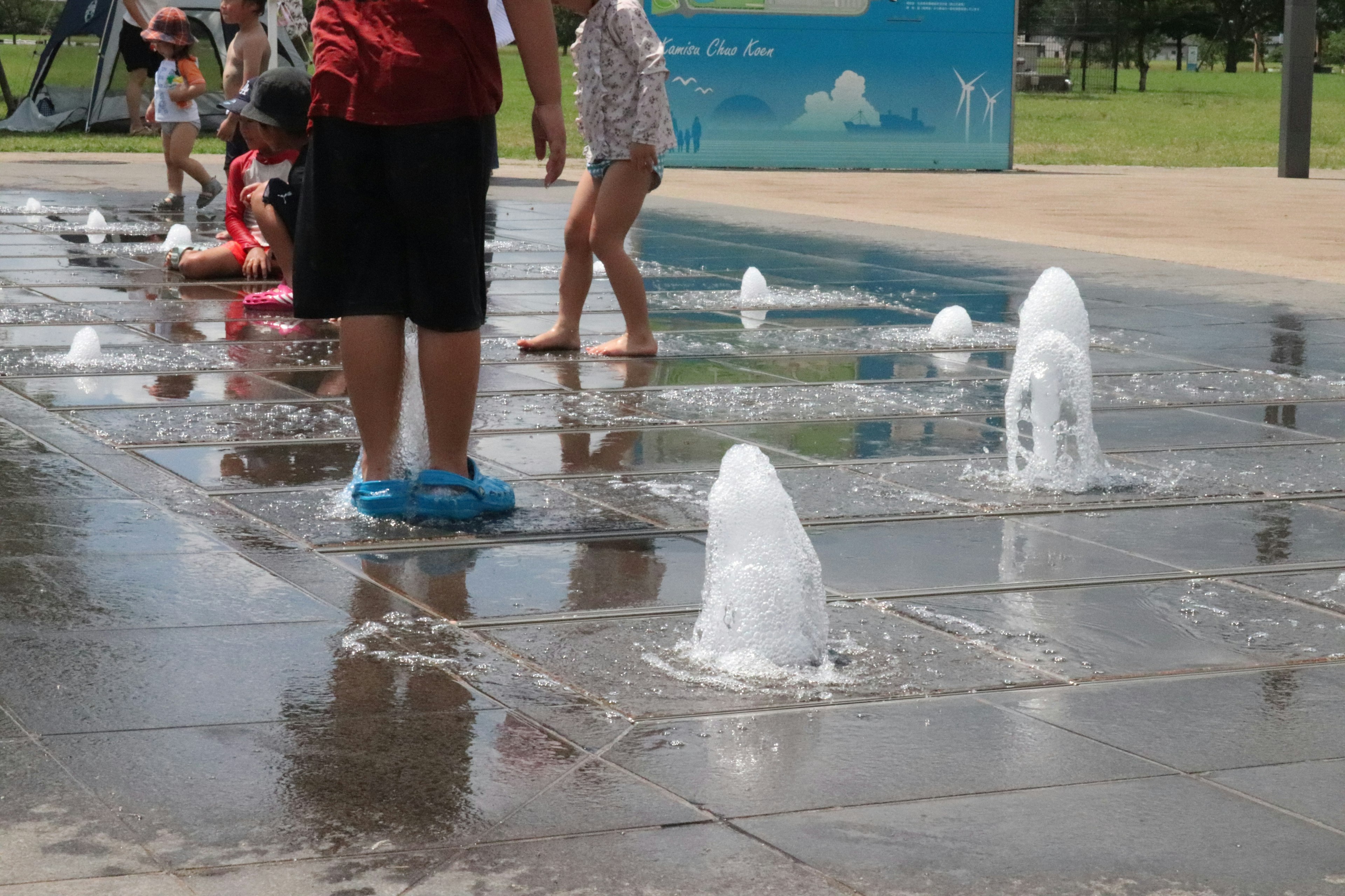 Kinder spielen in einem Wasserspielplatz mit Fontänen in einem Park