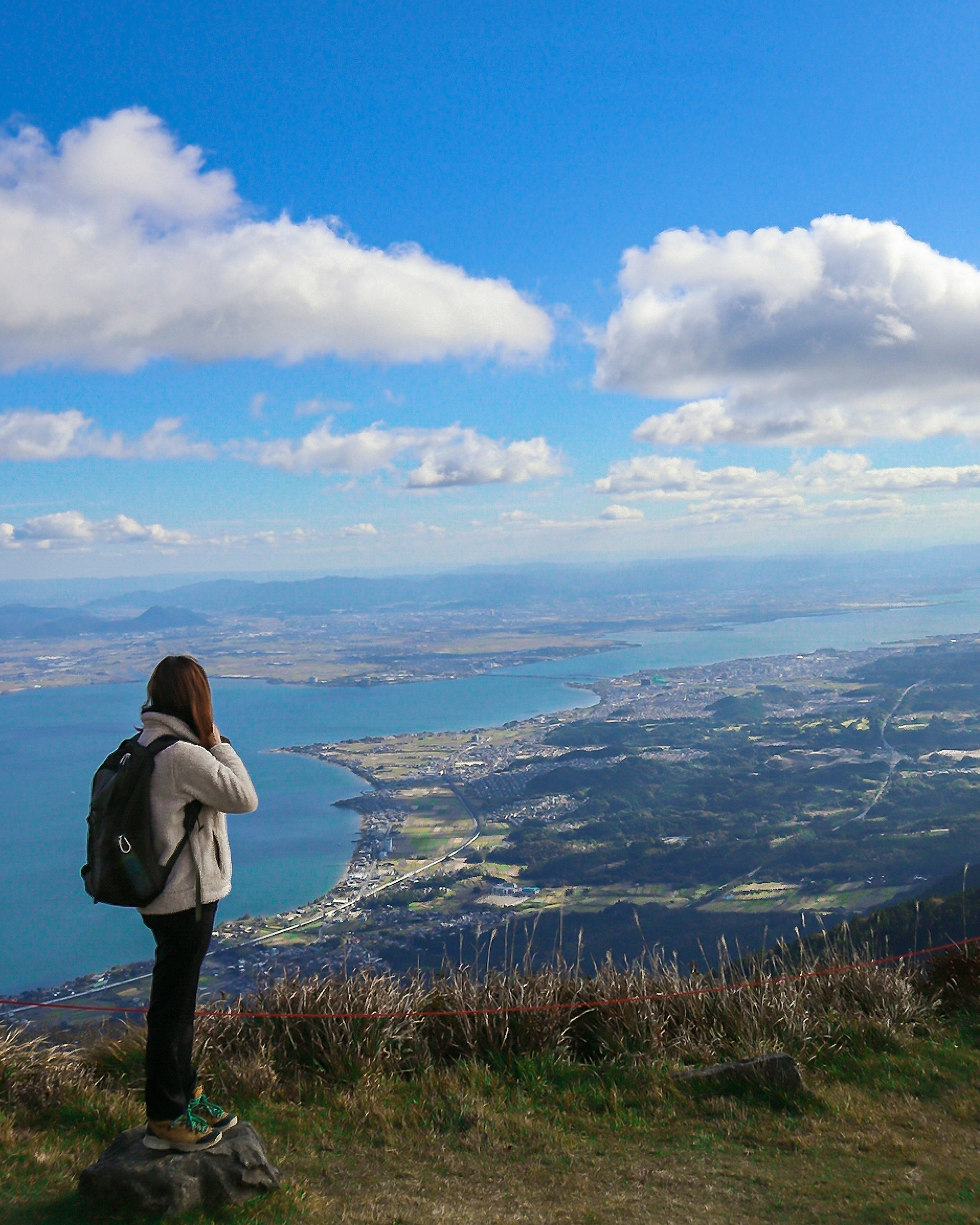 Woman standing on a mountain top overlooking a scenic view with blue sky and clouds