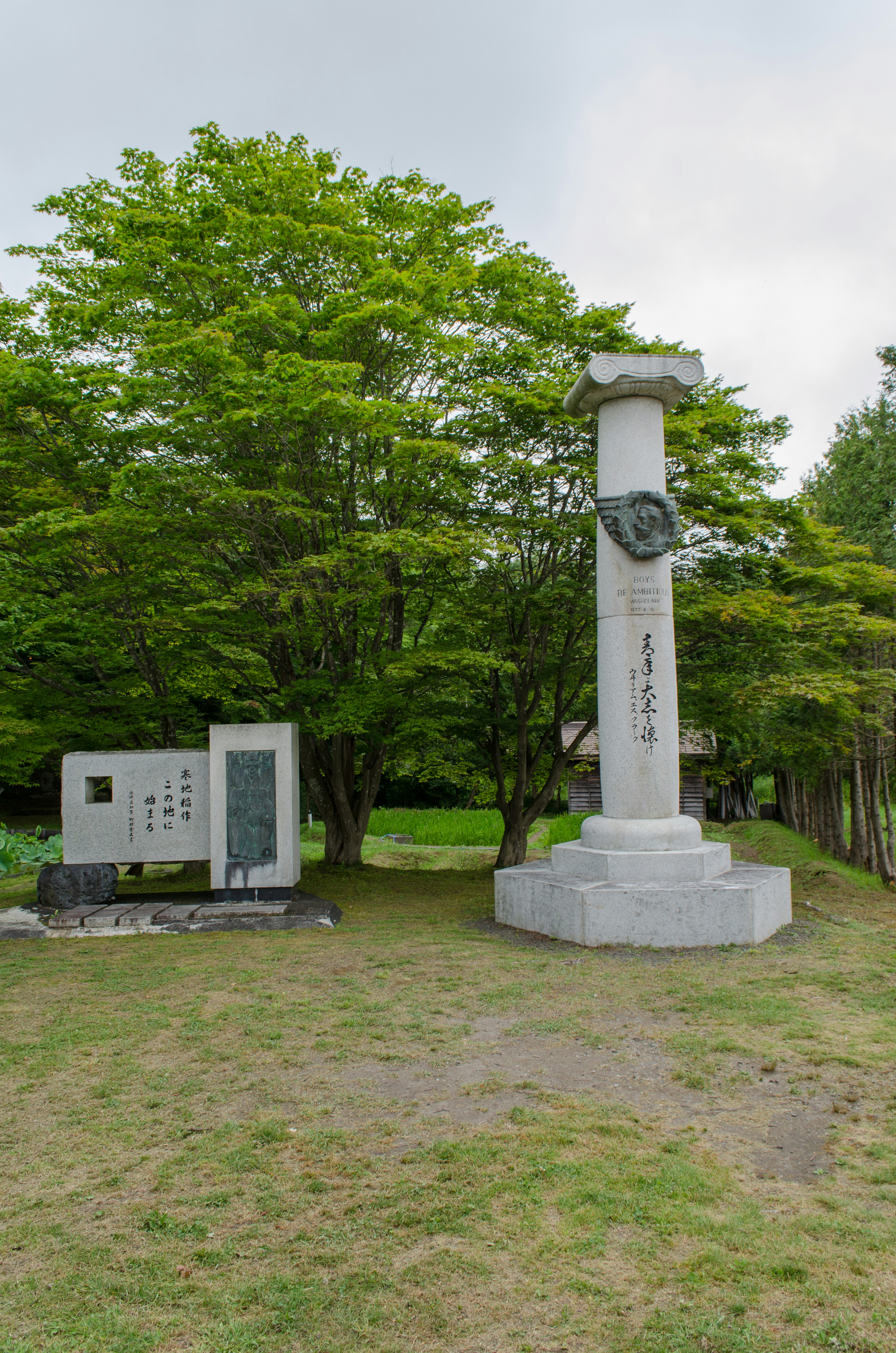 Monumen batu dan papan informasi di taman yang rimbun