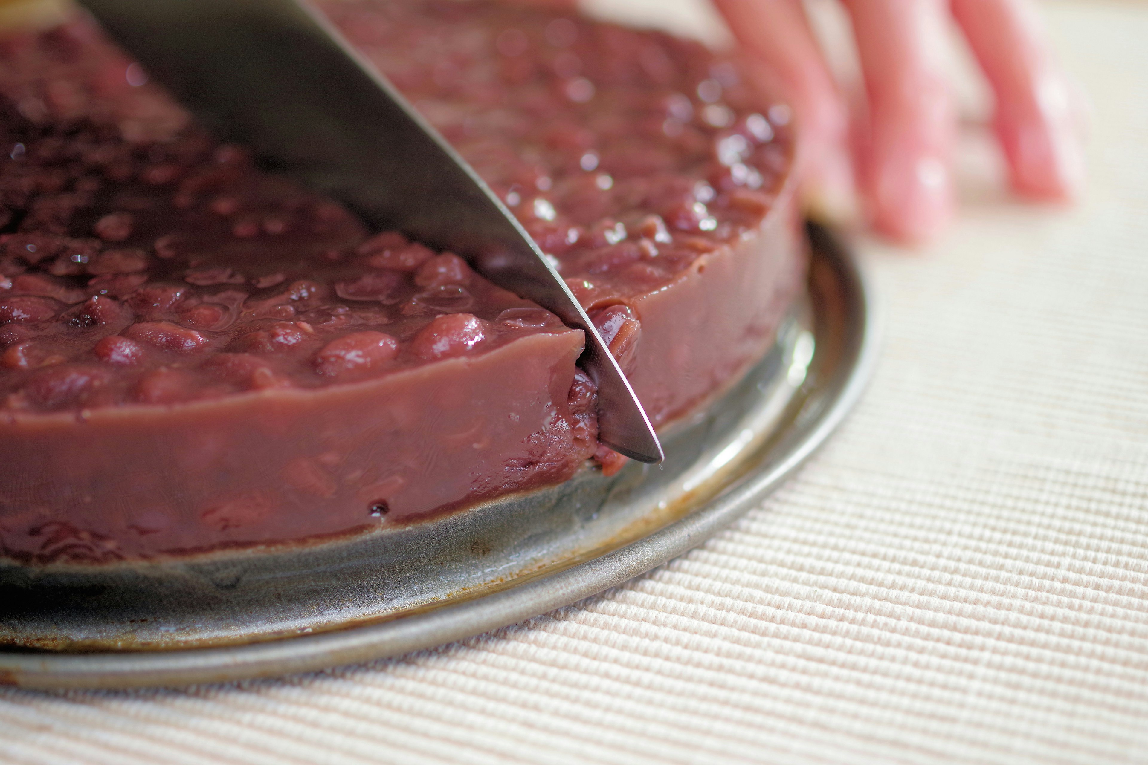 A hand cutting a red bean cake on a metal tray