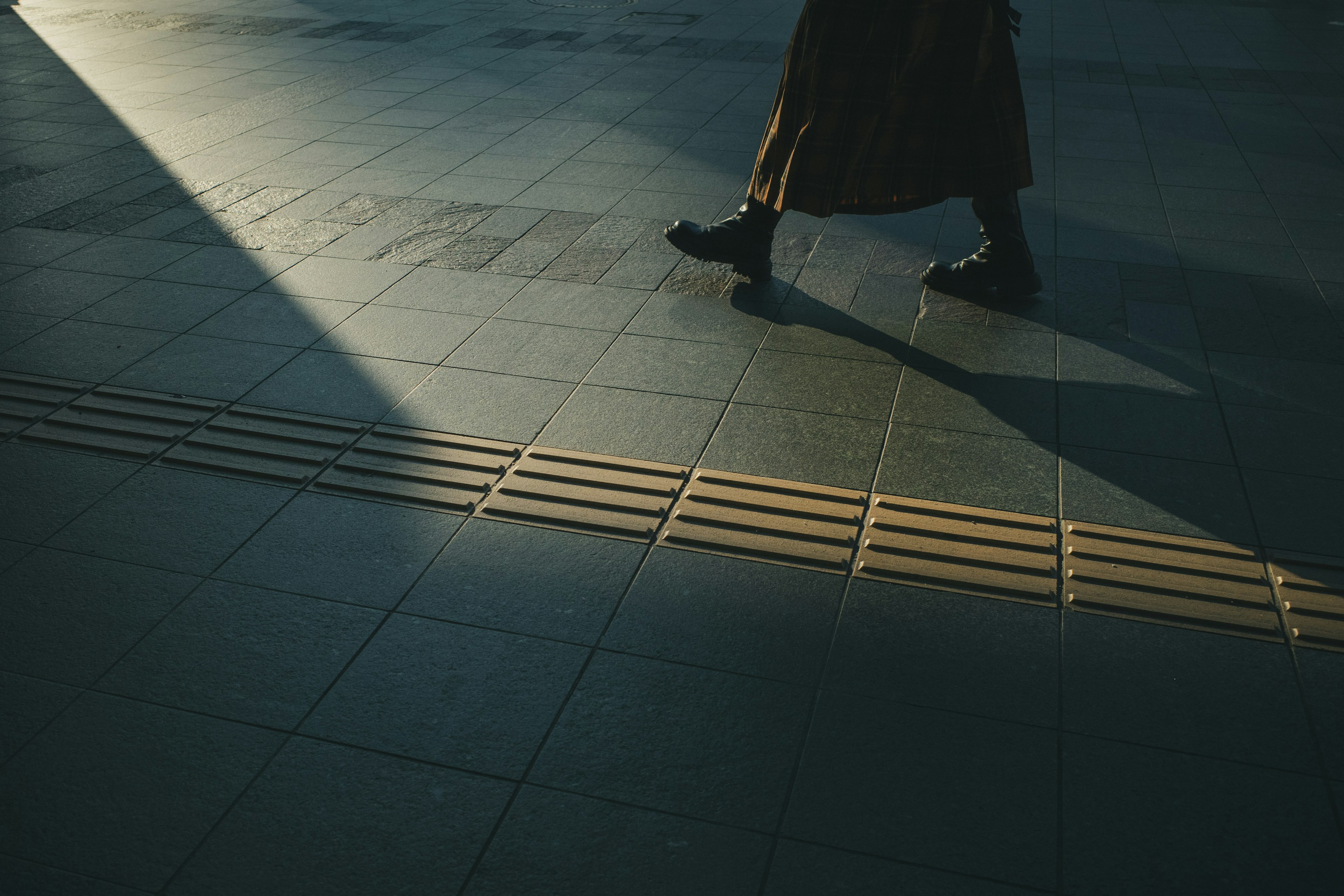 Persona caminando en la sombra con pavimento de baldosas y contraste de luz