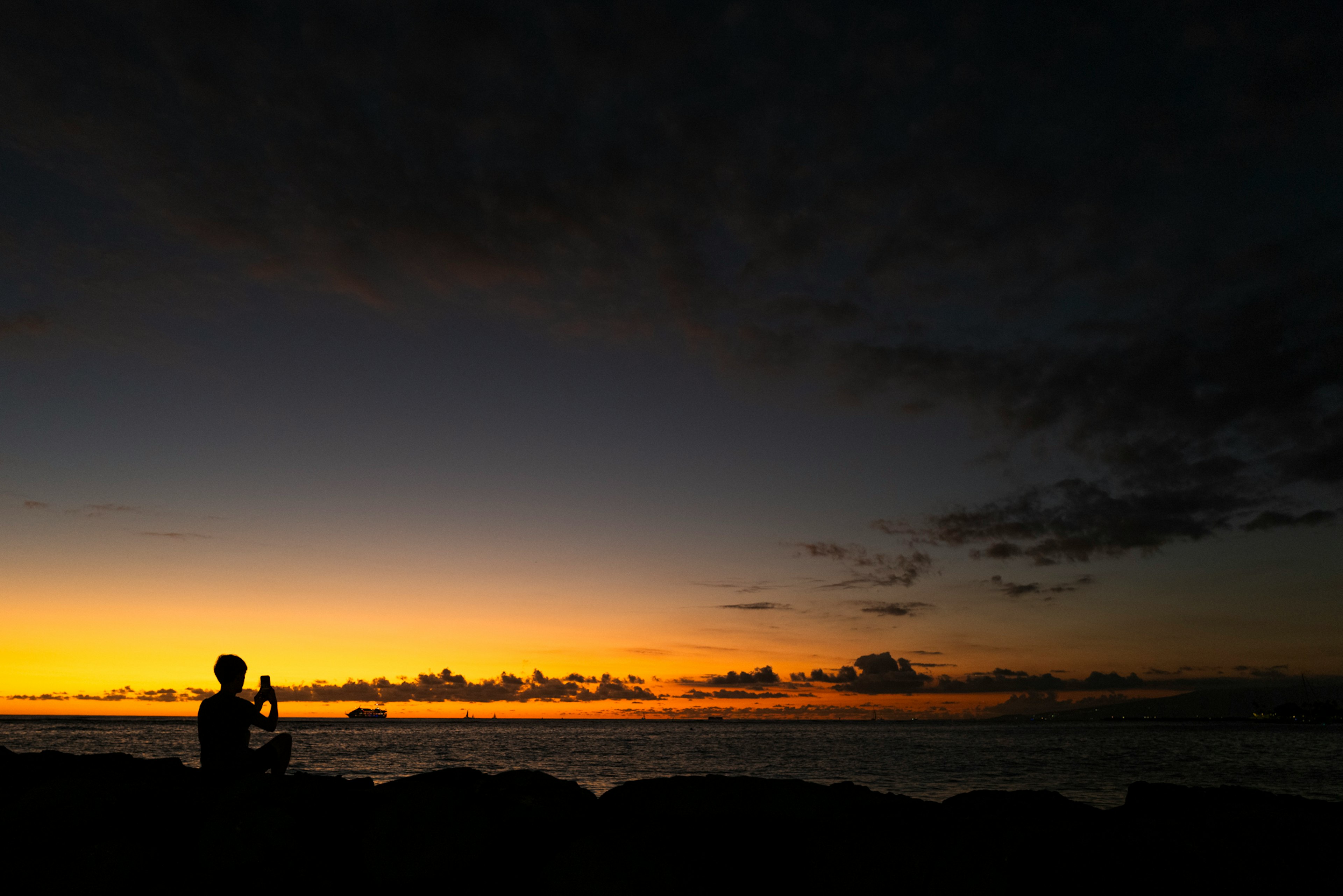 Silhouette einer Person, die ruhig gegen einen Sonnenuntergang sitzt, Ozean und Wolken schaffen eine schöne Landschaft