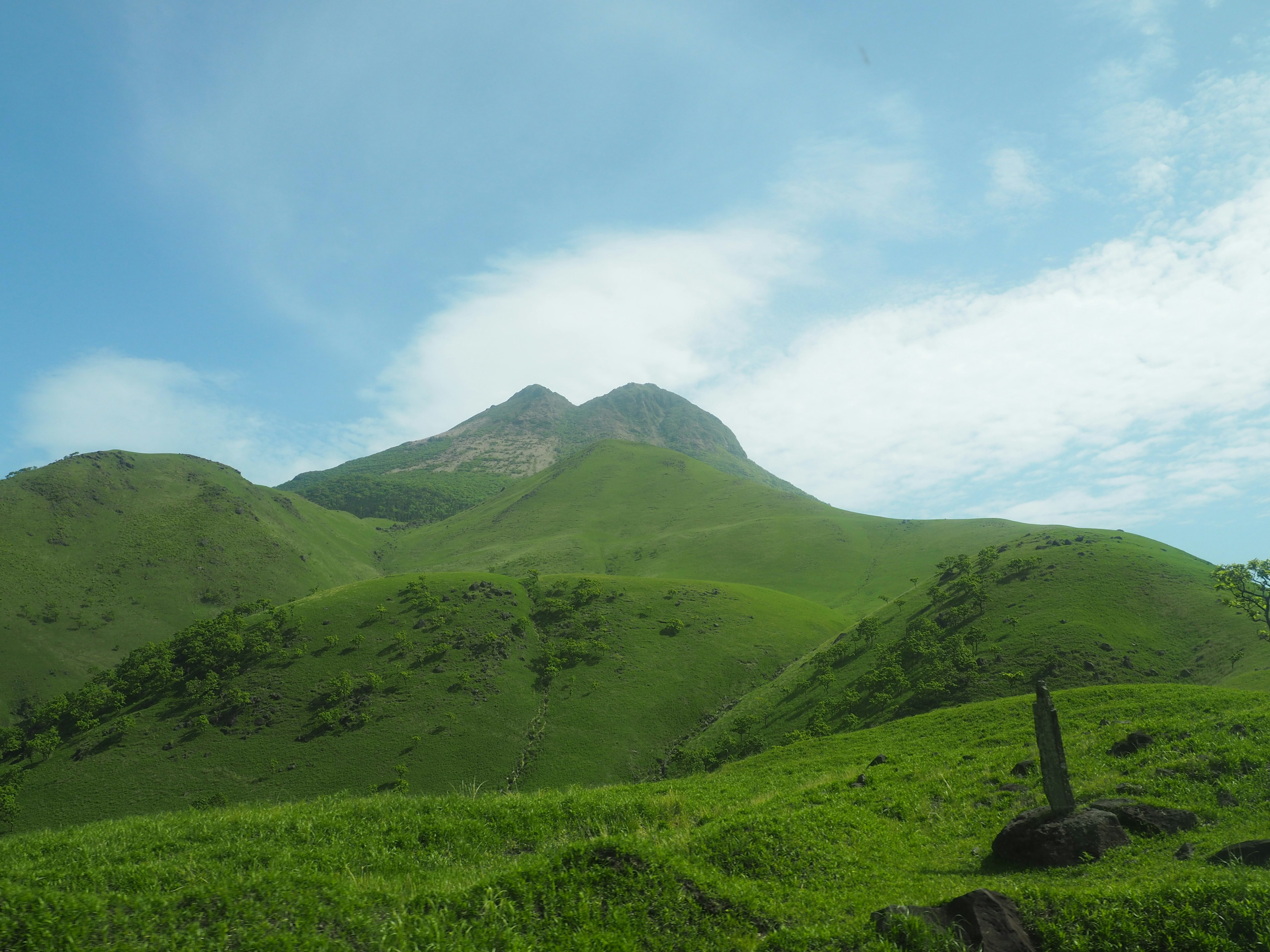 緑の丘と青空の下にそびえる山の風景