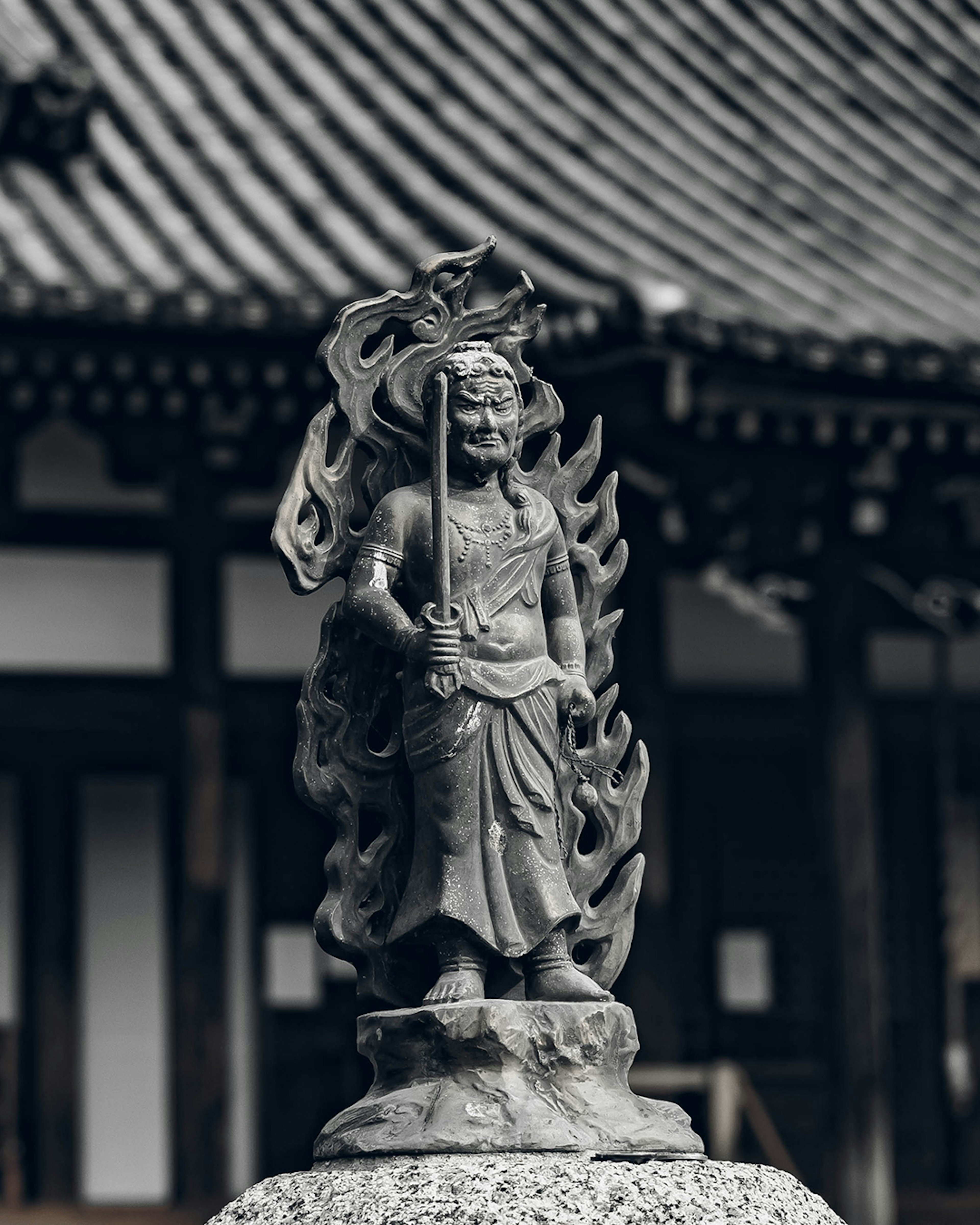 Statue of a deity holding a flame with traditional roof architecture in the background