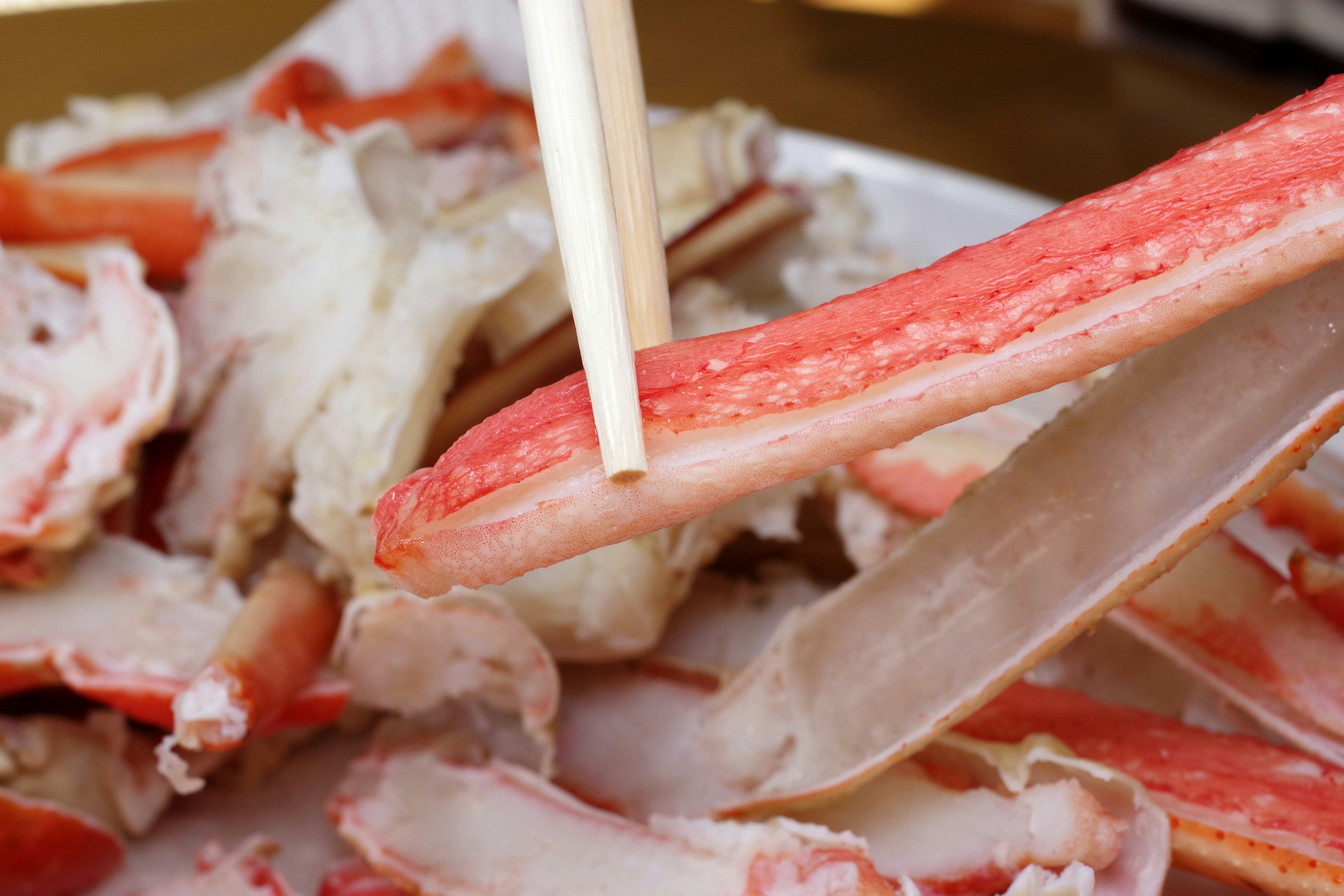 Stäbchen, die Krabbenfleisch greifen, mit weggeworfenen Krabbenschalen im Hintergrund