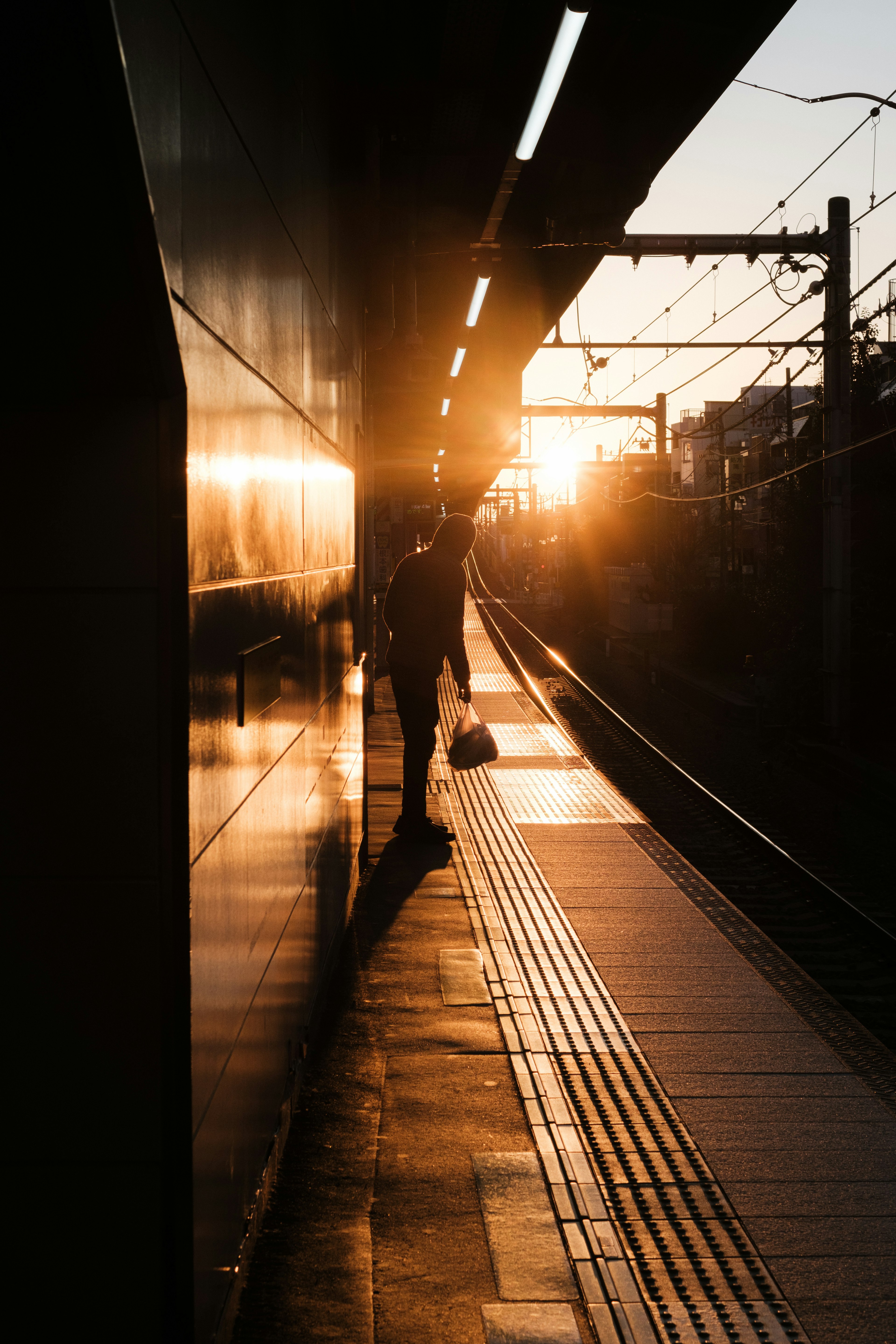 Silhouette of a person standing on a train platform with sunset in the background