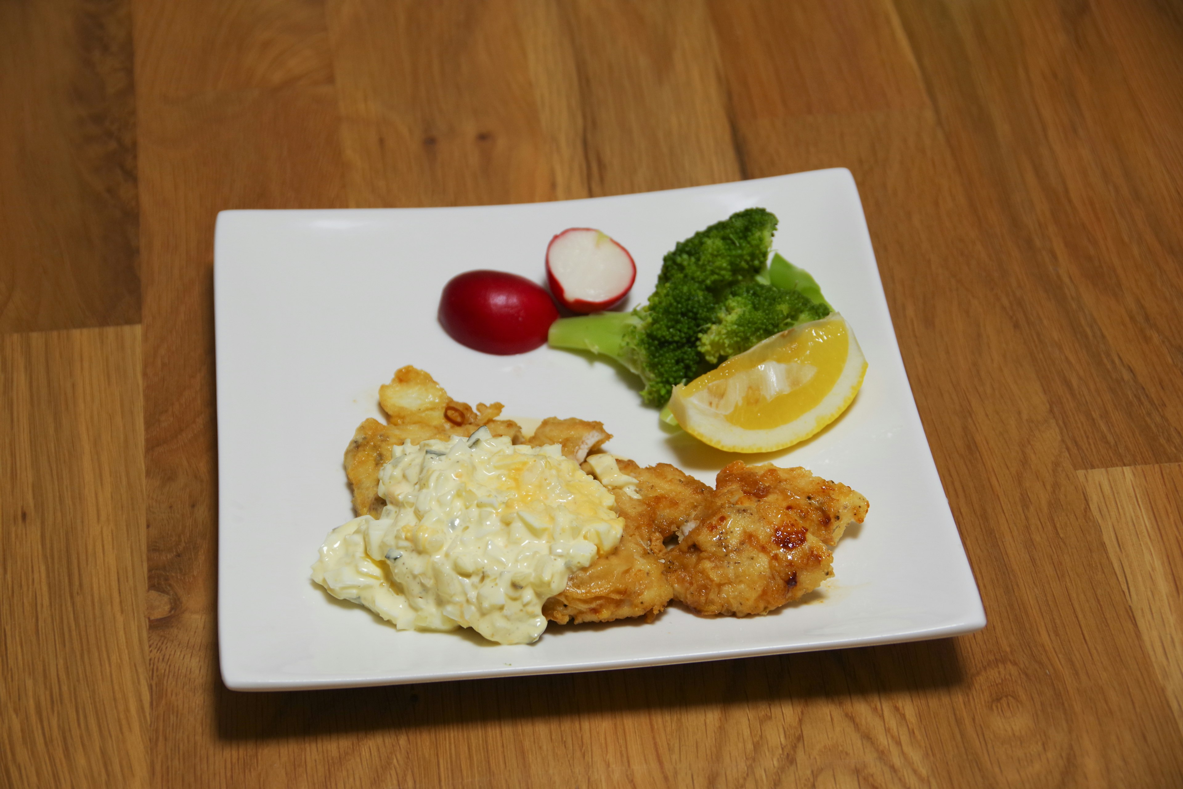 Pollo fritto con insalata di patate, lattuga, limone e ravanello su un piatto bianco