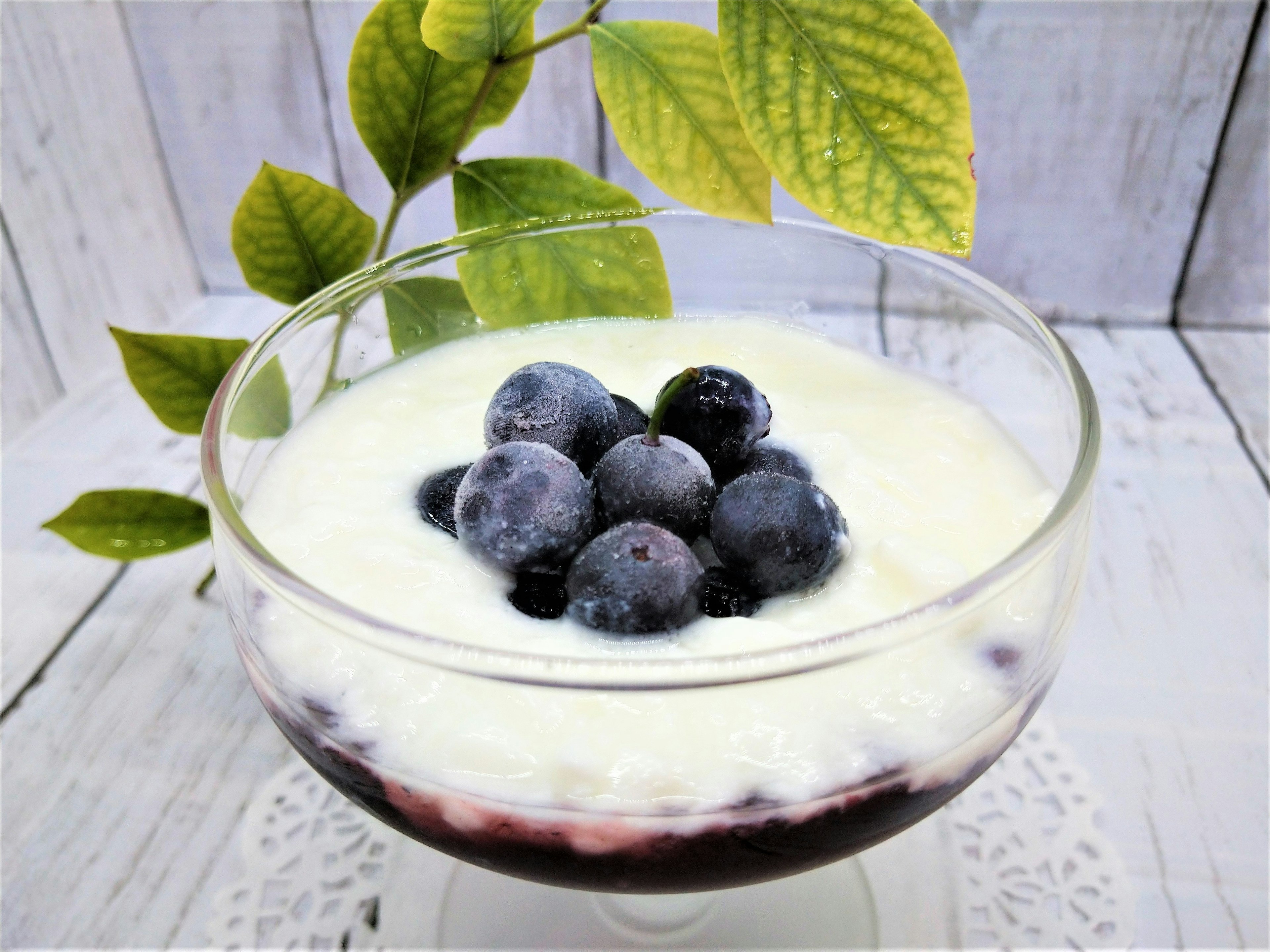 Puding dalam mangkuk kaca dihiasi krim dan blueberry