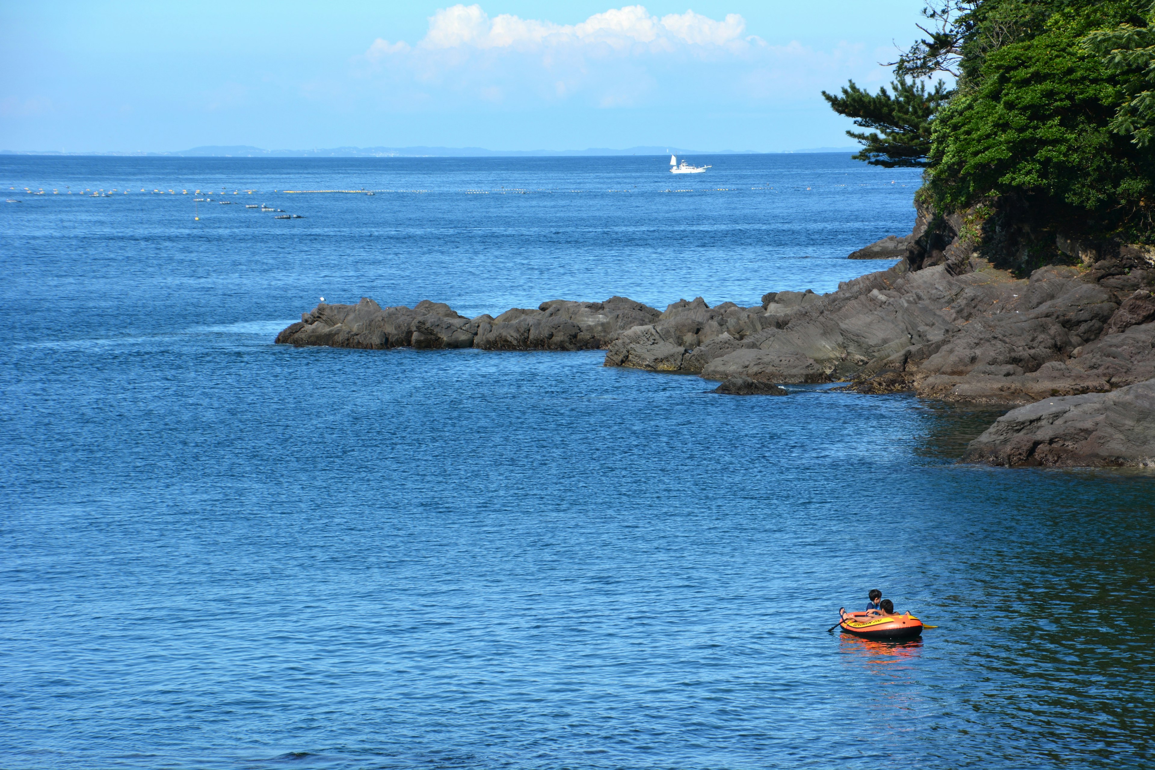 Kayak arancione sull'acqua blu vicino a una costa rocciosa con una barca a vela lontana