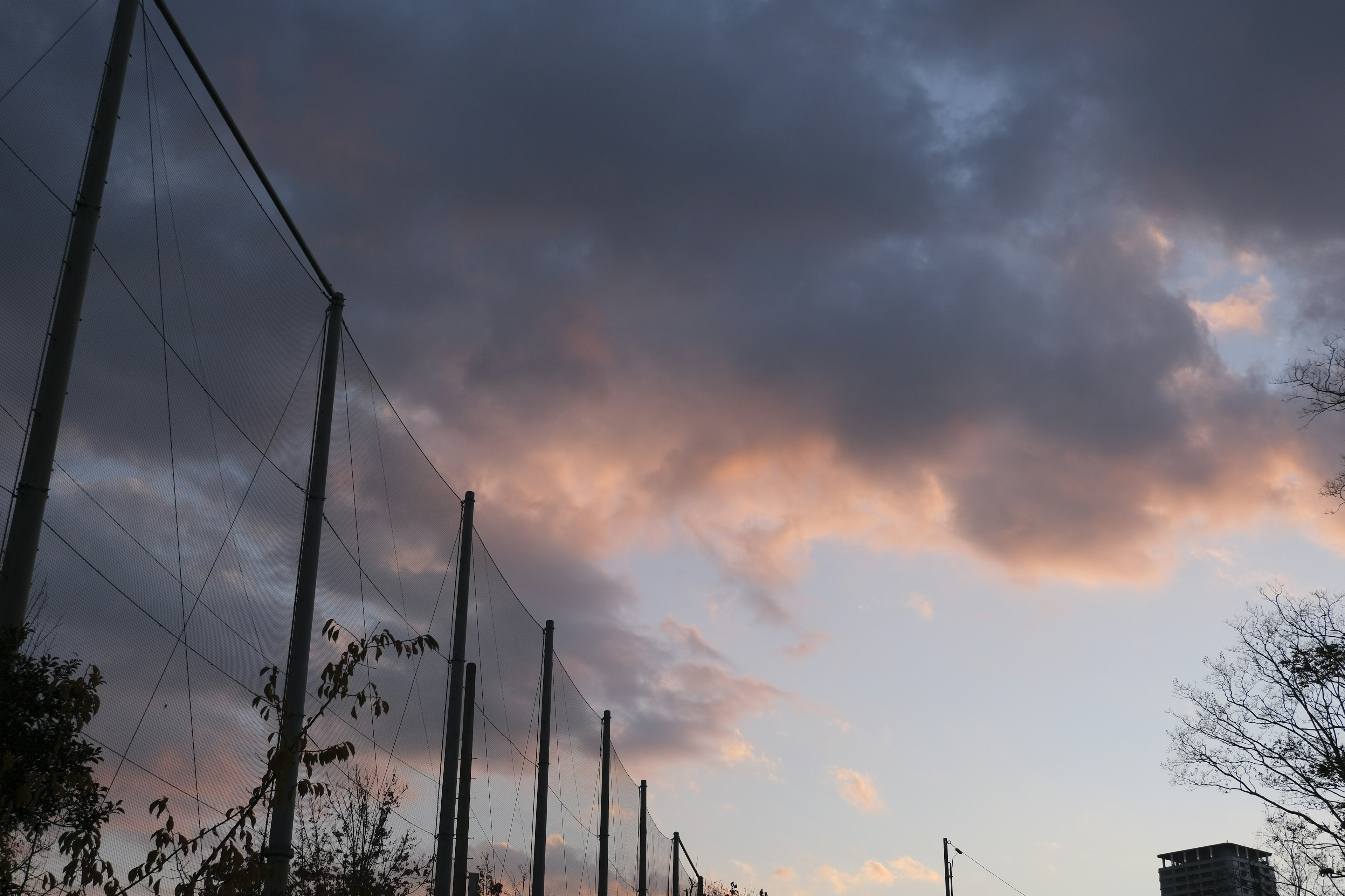 曇り空と夕焼けのオレンジ色が混ざる風景とフェンス