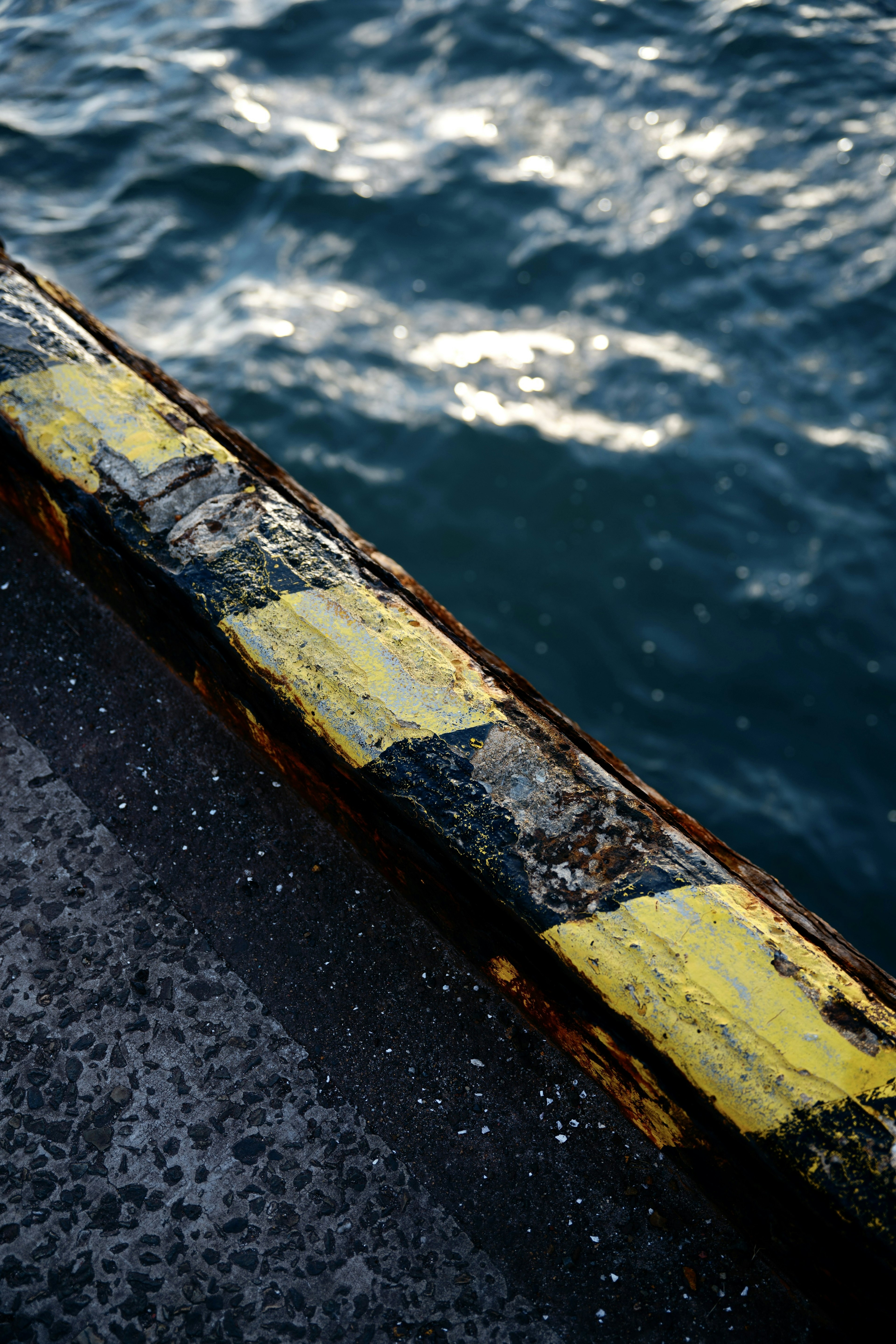 Acercamiento de una barandilla de muelle rayada de amarillo desgastada reflejando la luz en la superficie del agua