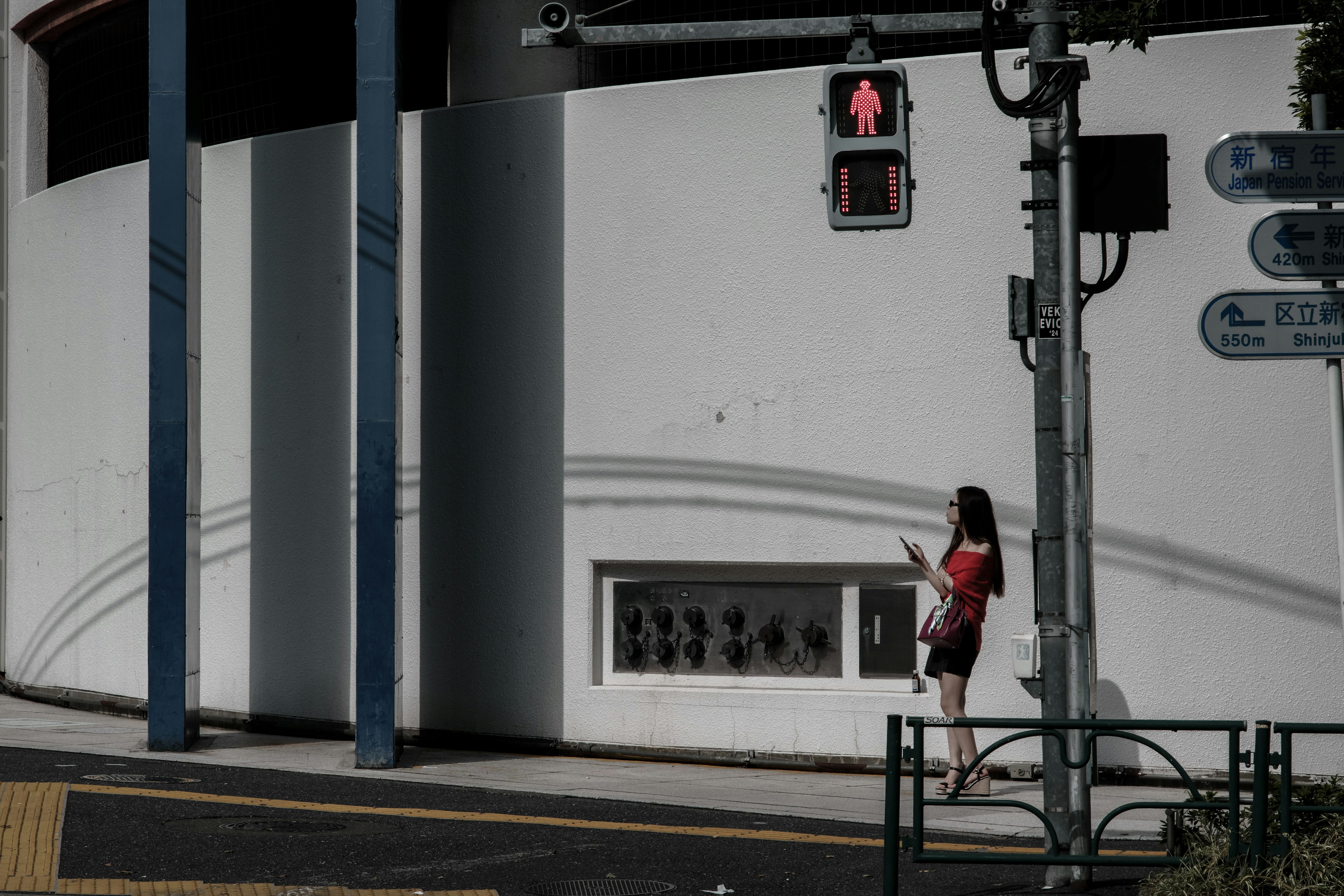 Una mujer de pie en un semáforo rojo junto a una pared blanca