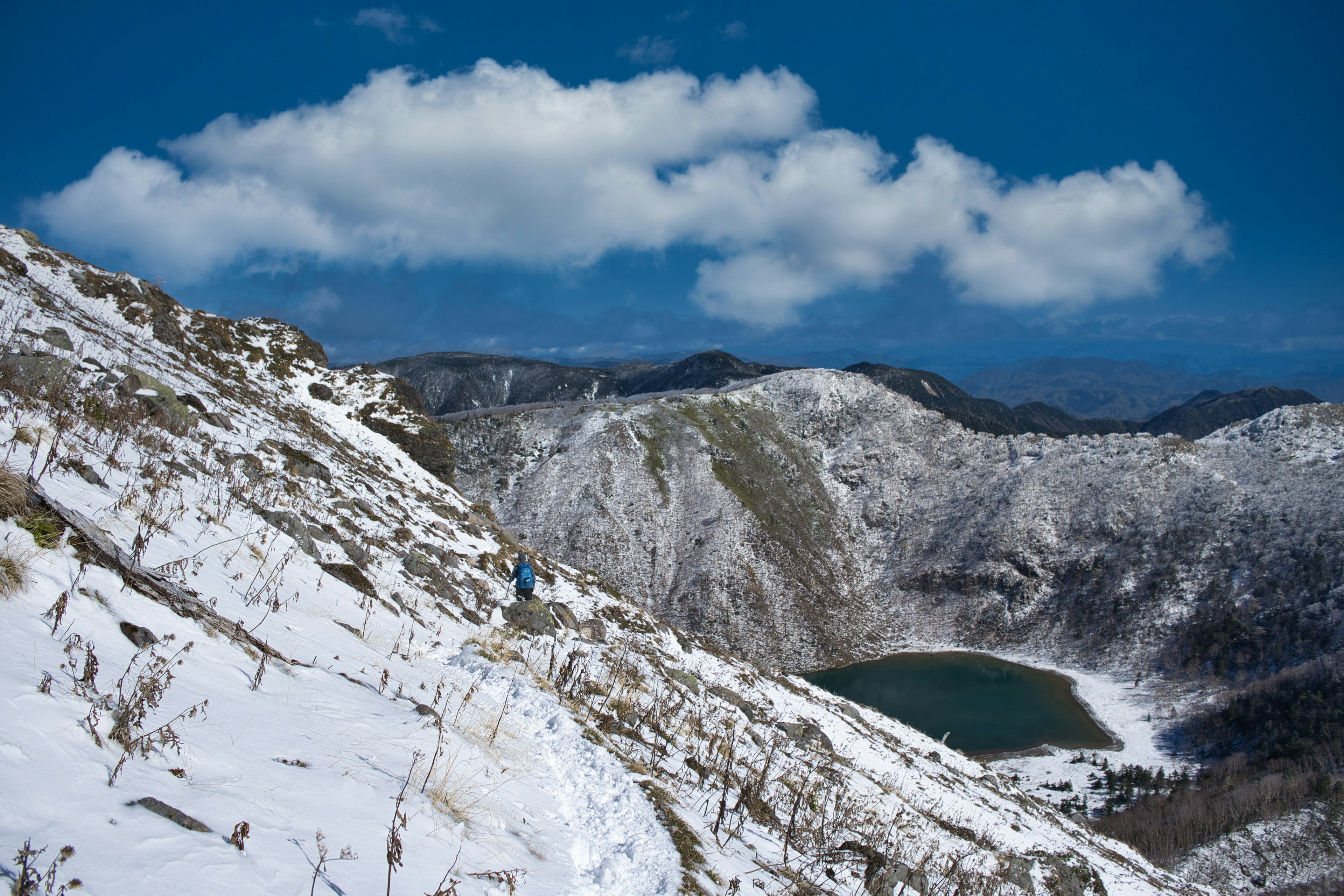 Snow-covered mountain slope with a visible lake and blue sky