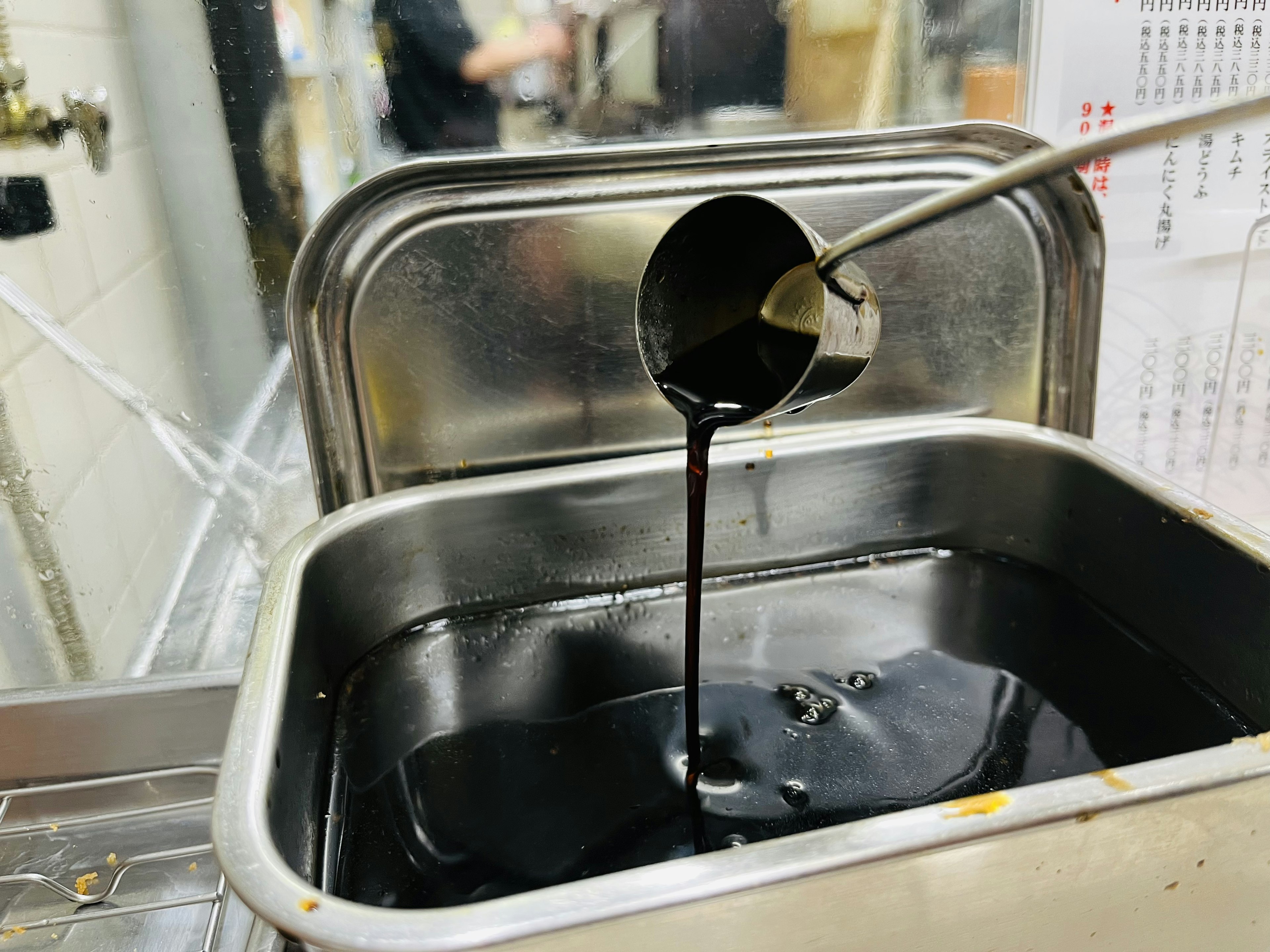 Immagine di un cucchiaio che versa un liquido nero in un contenitore metallico