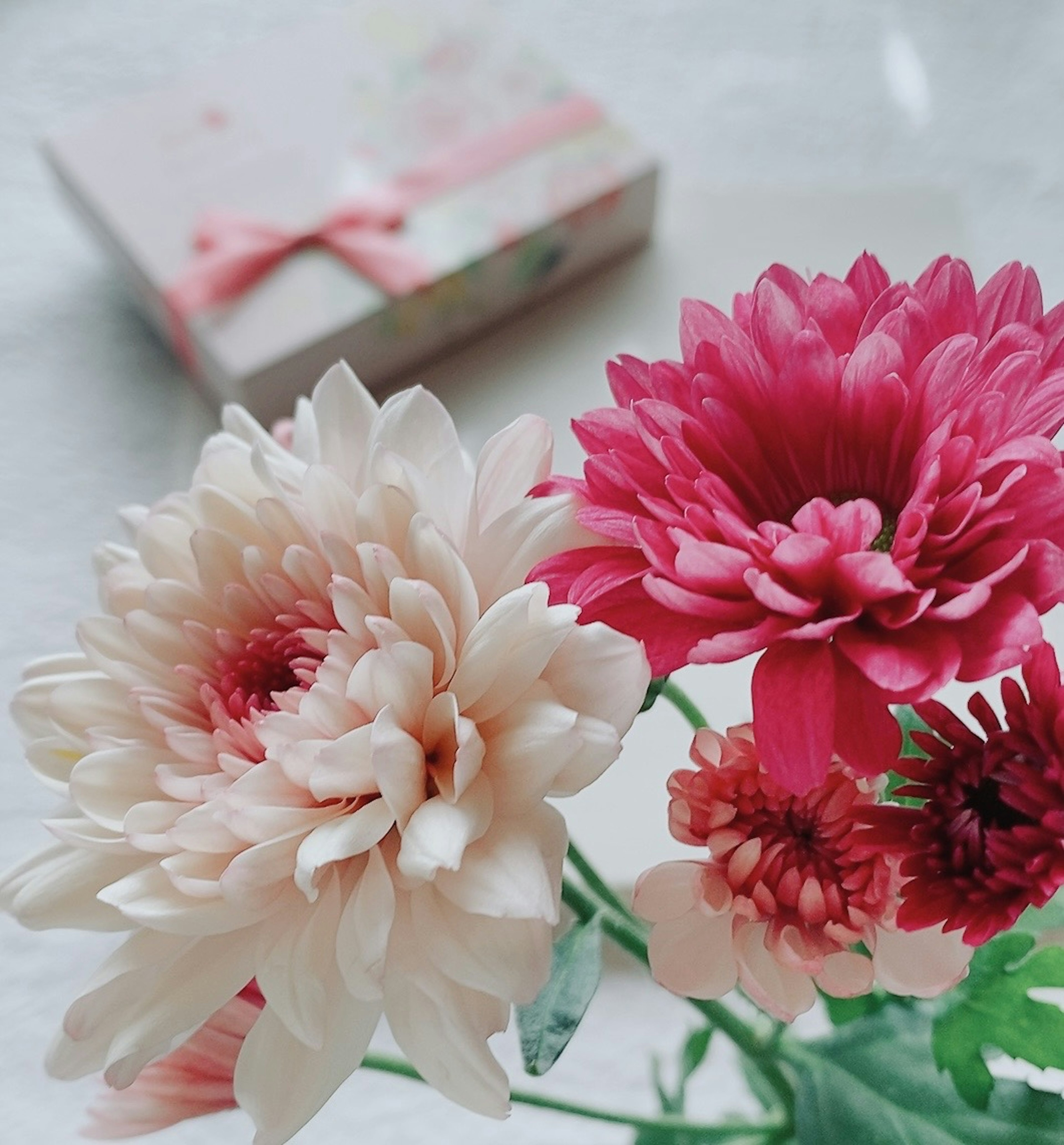 Strauß aus rosa und cremefarbenen Blumen mit einer verpackten Geschenkbox im Hintergrund