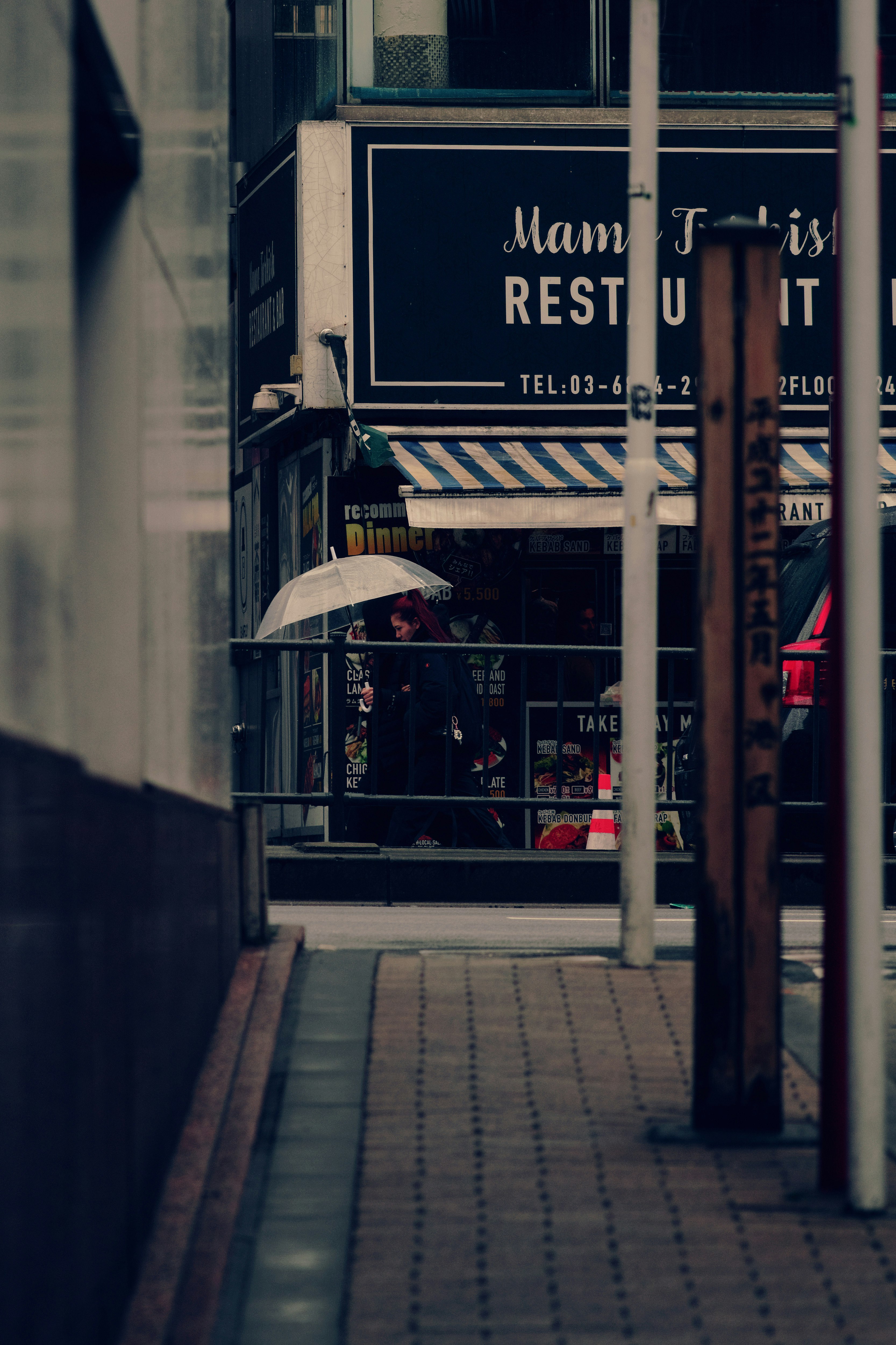 Street corner with restaurant sign and person holding an umbrella