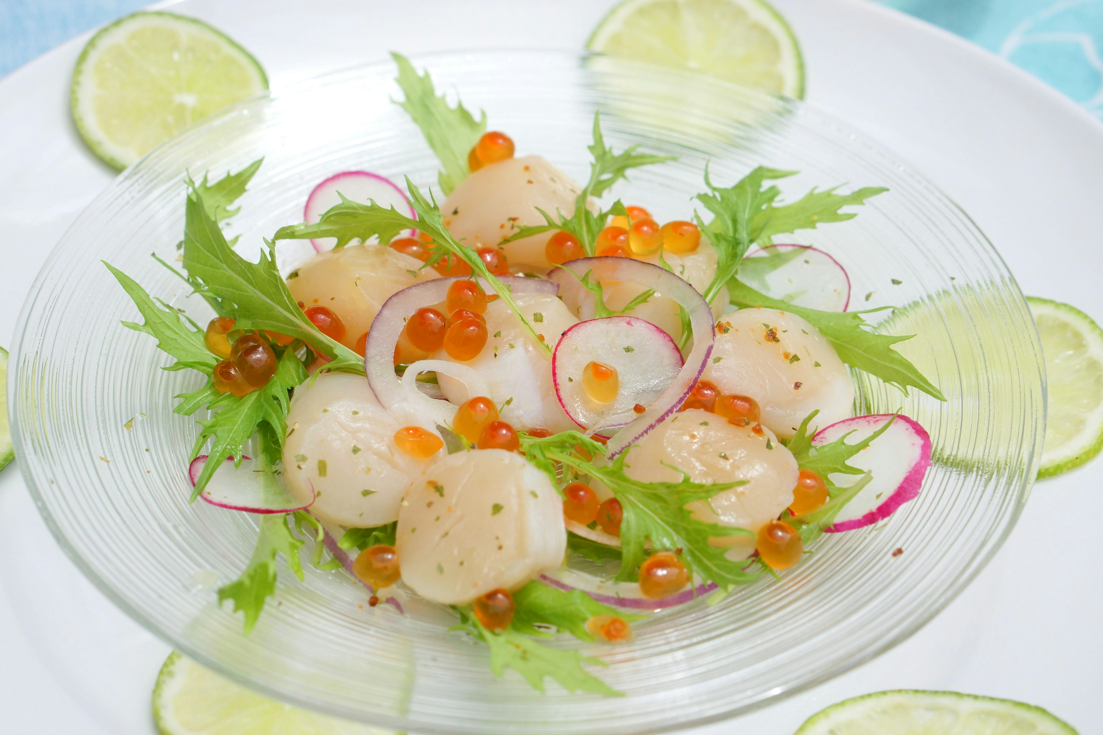 Salade de coquilles Saint-Jacques fraîches et de caviar de saumon présentée avec des tranches de citron vert et des herbes