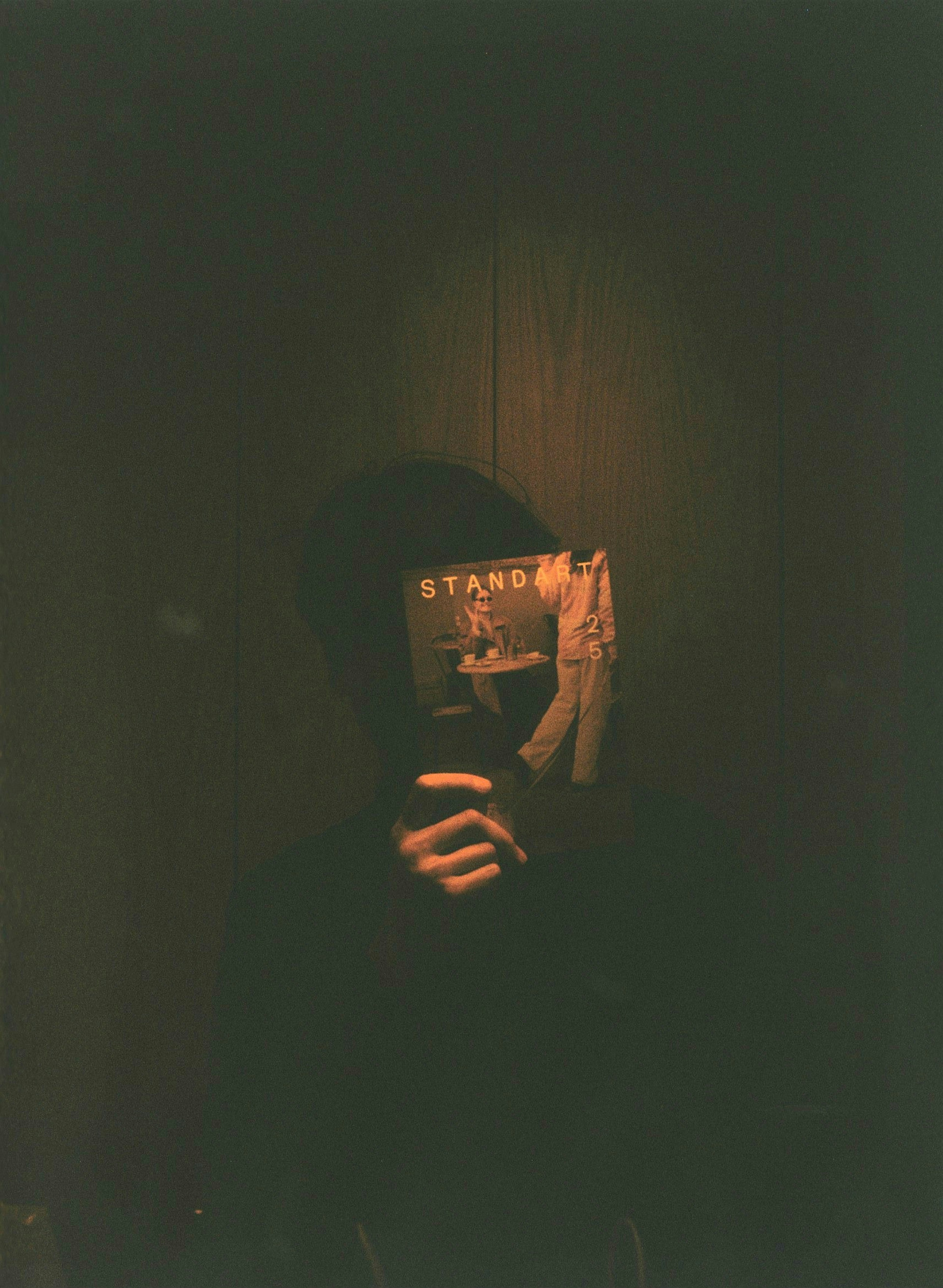 A person holding a book in front of their face with a dark background