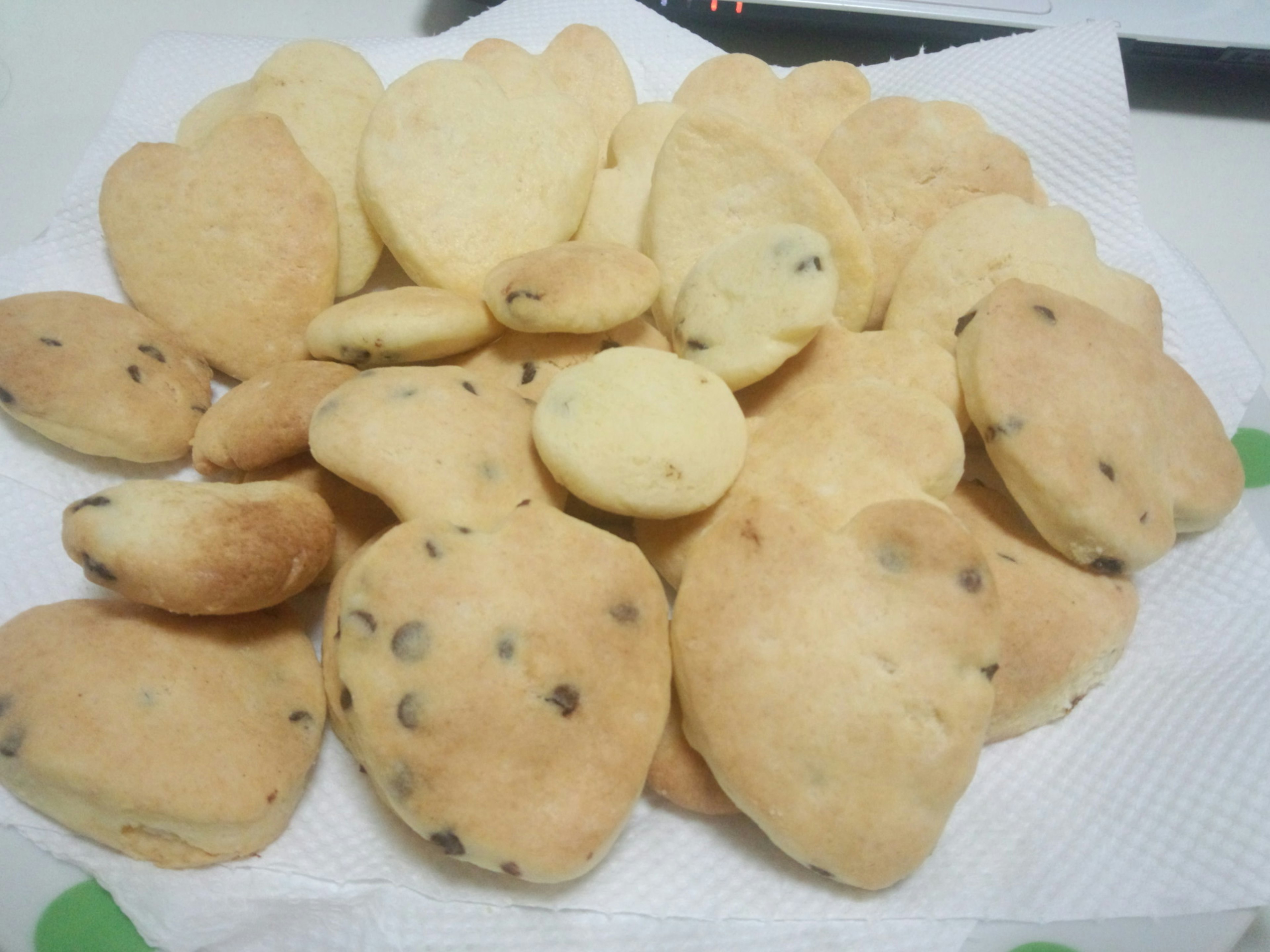 A pile of cookies in various shapes and sizes including some with chocolate chips