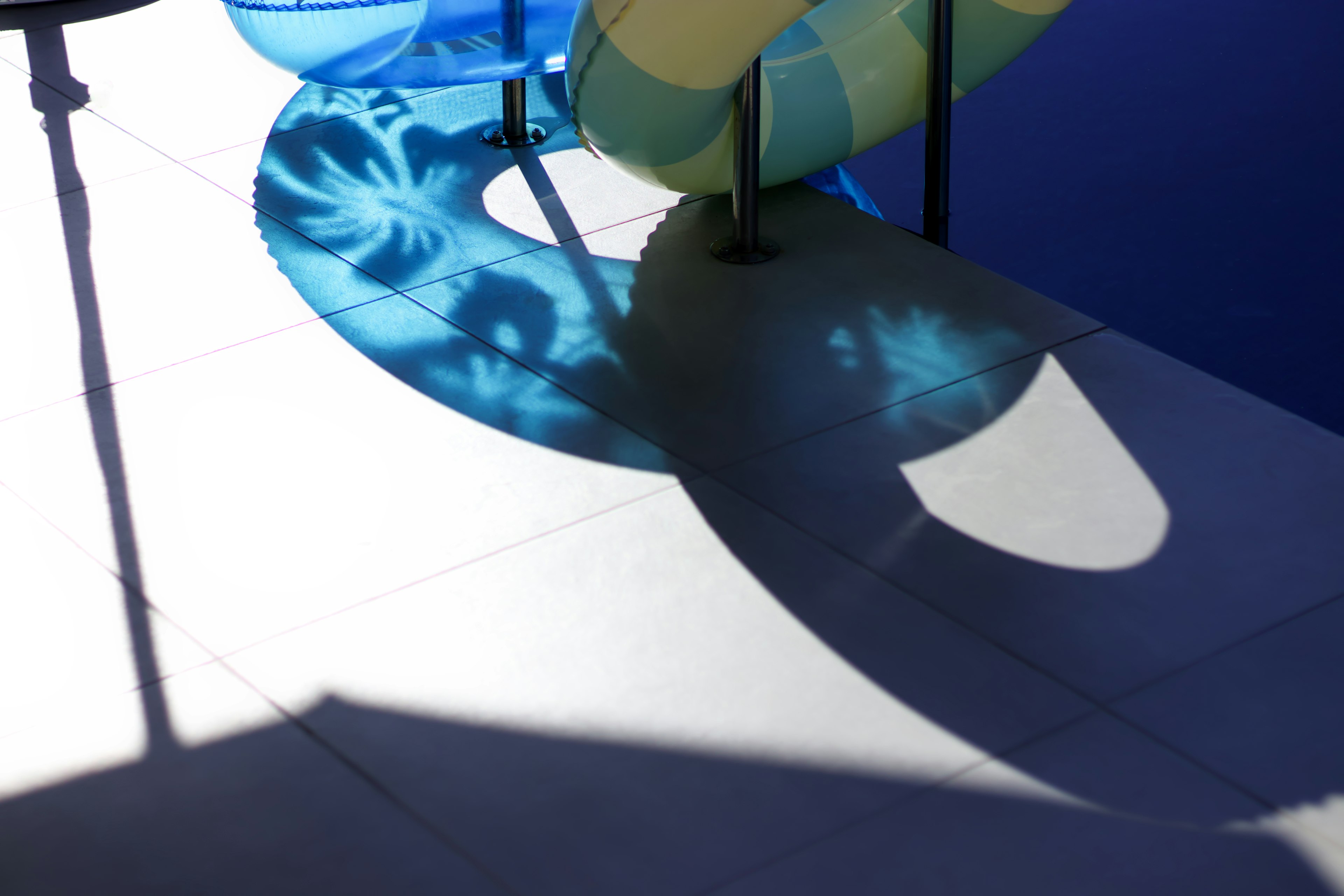 Blue and yellow pool floats casting shadows on the deck