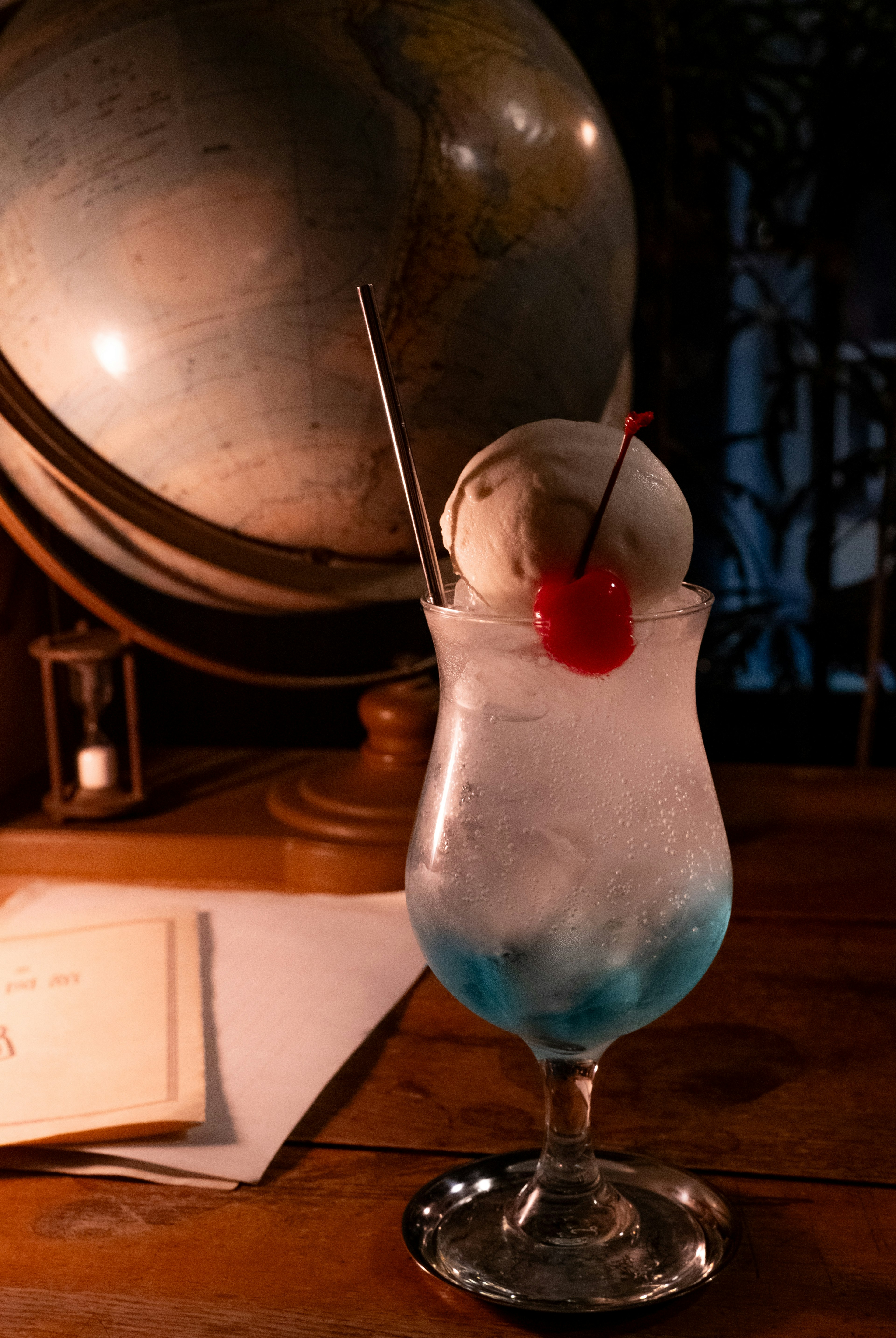 A blue cocktail glass topped with ice cream and a cherry beside a globe