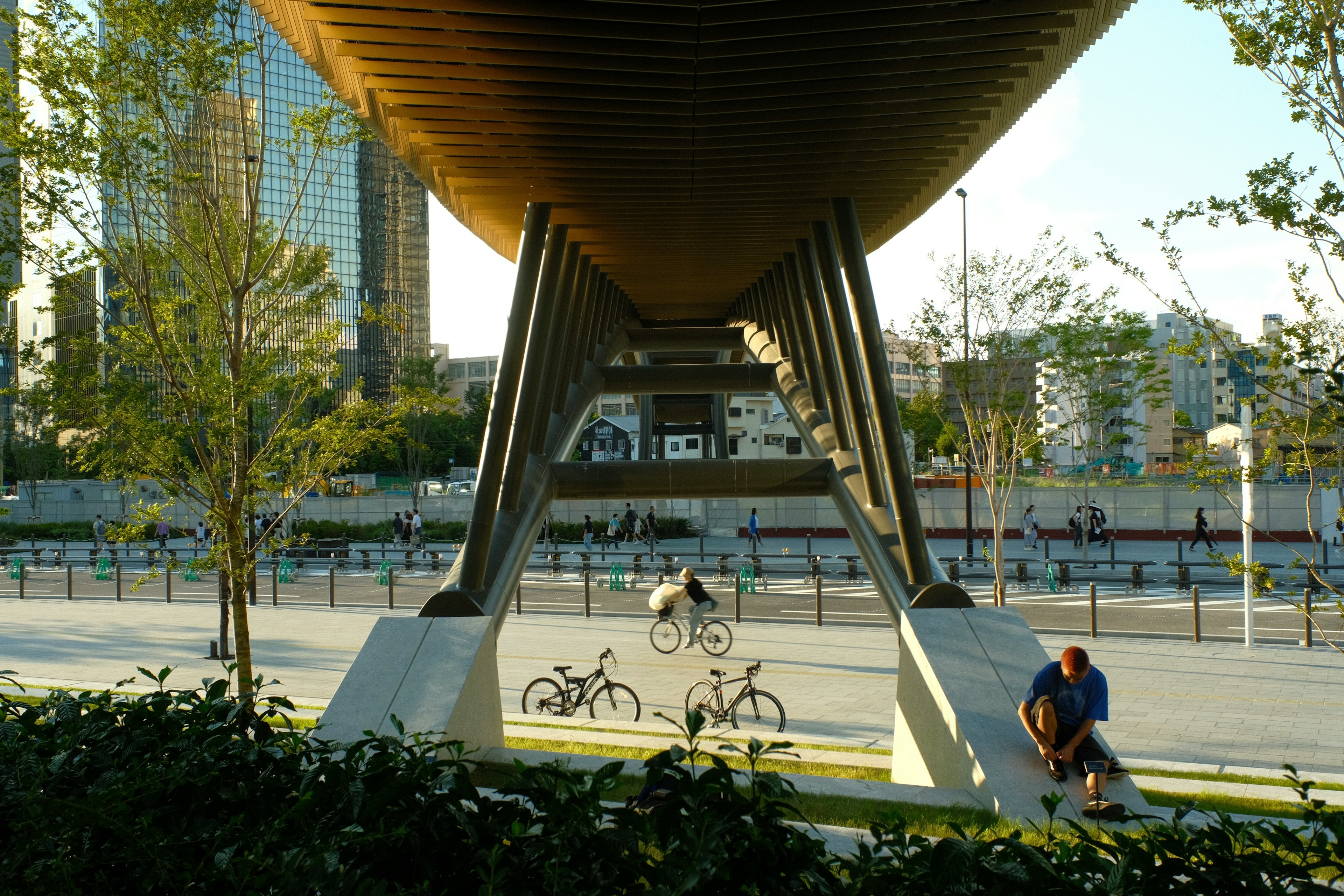 ทัศนียภาพในเมืองที่มีชายคนหนึ่งนั่งอยู่ใต้สะพานสมัยใหม่และจักรยานใกล้เคียง