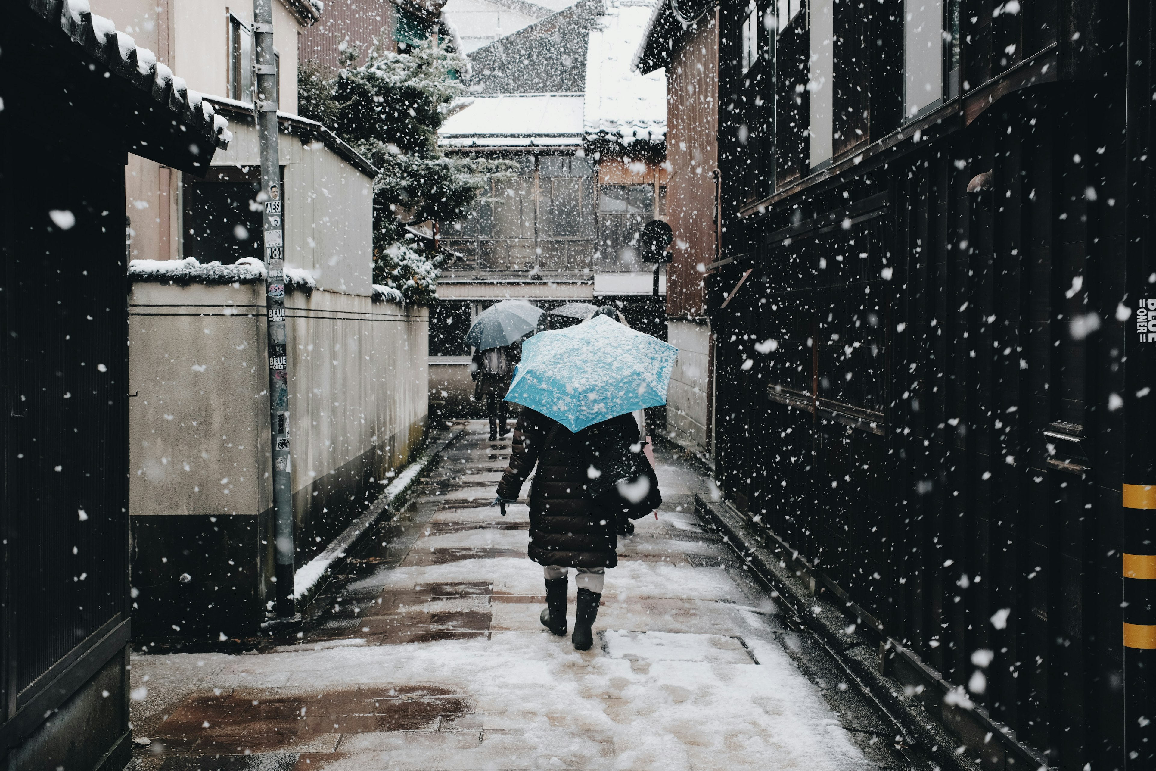 雪の中を歩く人と青い傘のある狭い通り