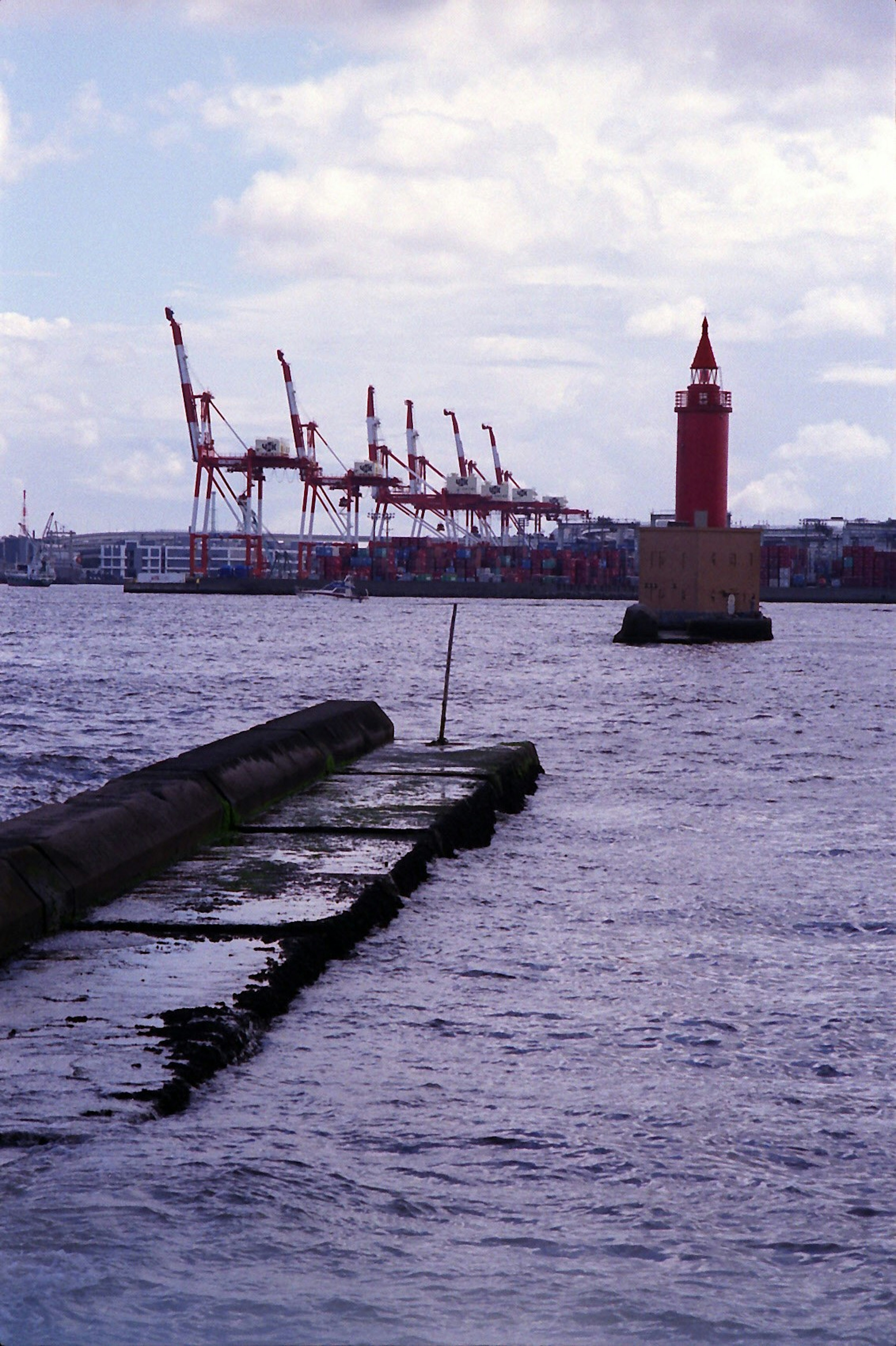 A red lighthouse with cranes in the background by the sea