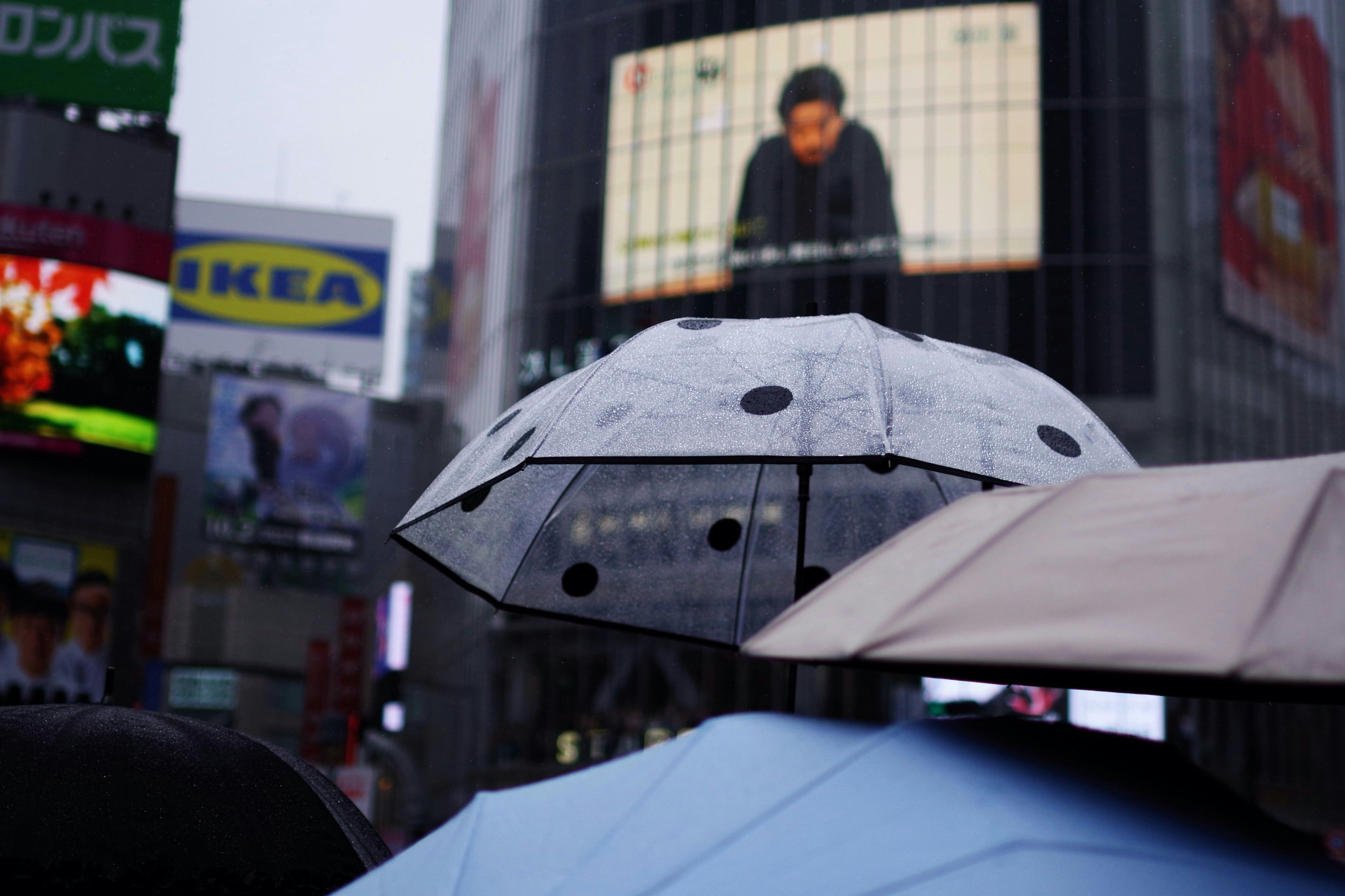 雨の中の傘と大きな広告ビジョンが映る都市の景観