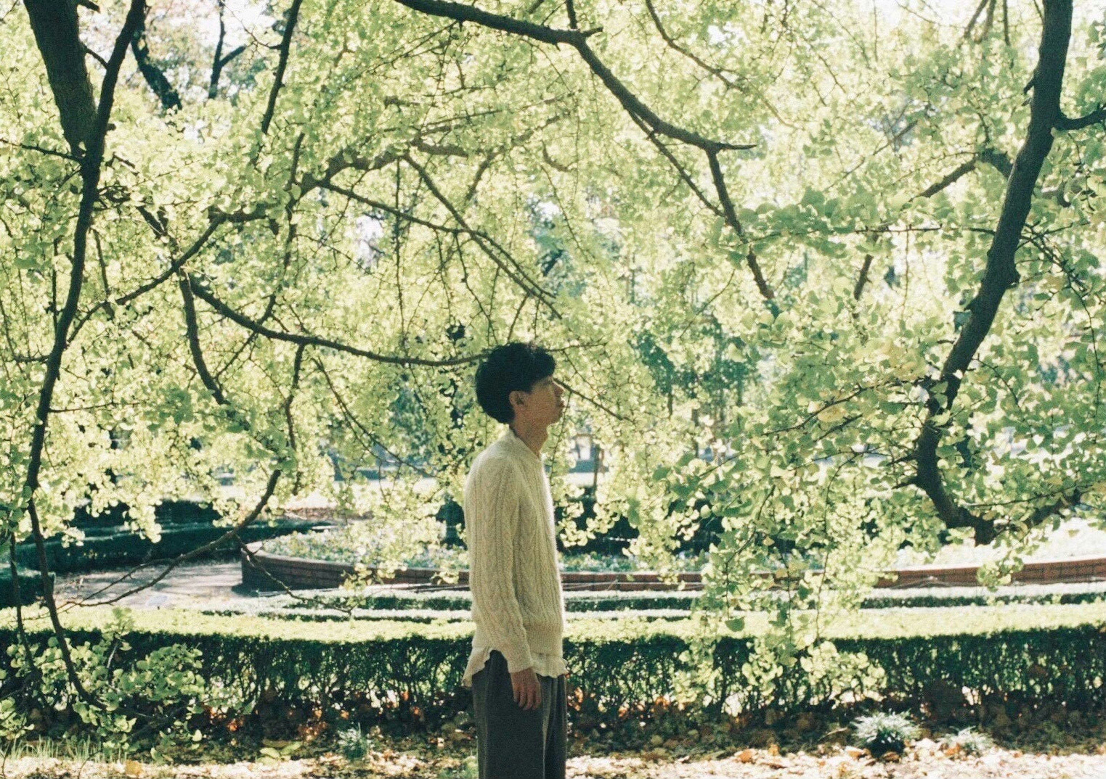 Side profile of a man standing under green trees