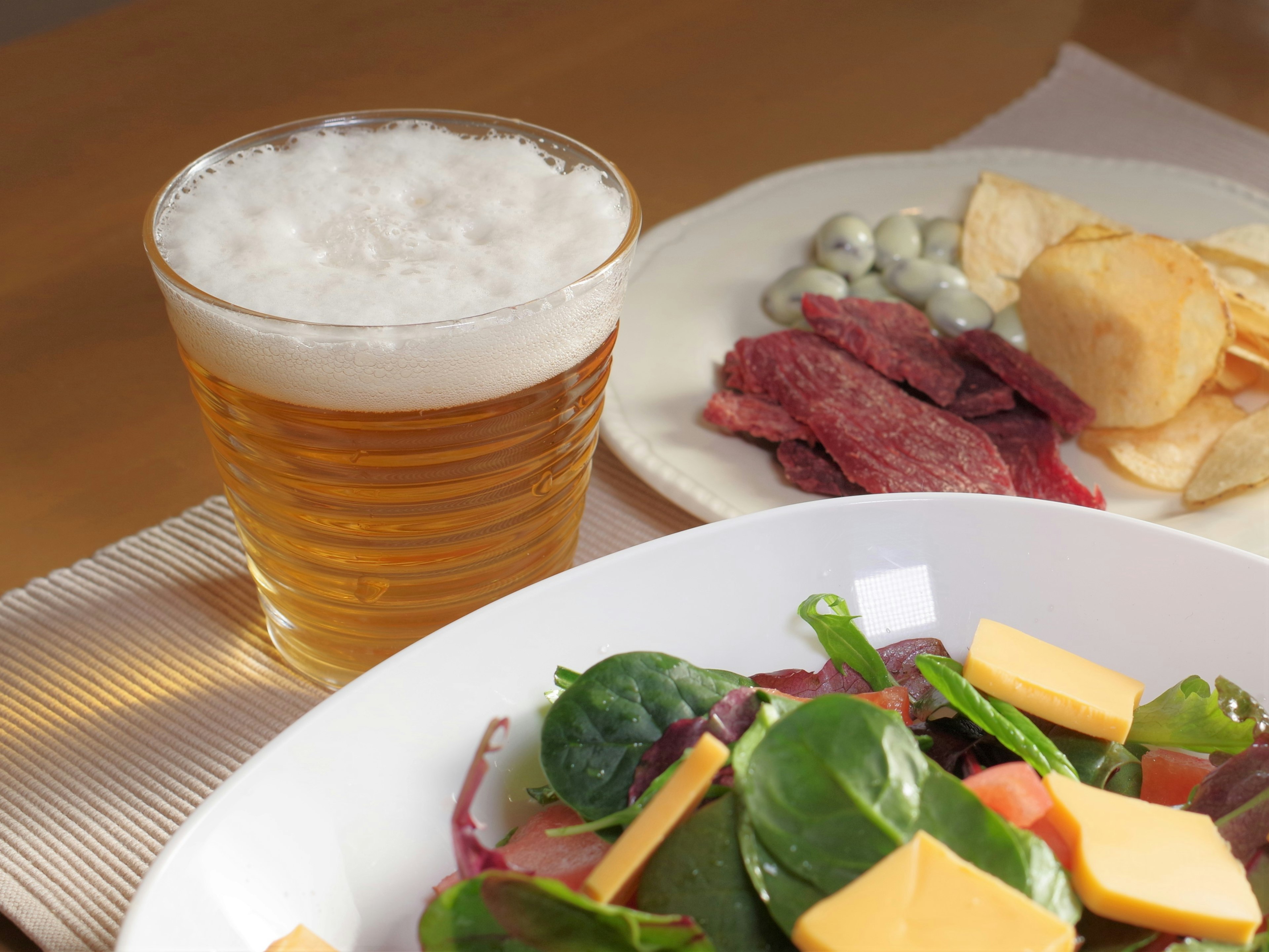 Ein lebhafter Salat mit Käse neben einem Glas Bier und verschiedenen Snacks