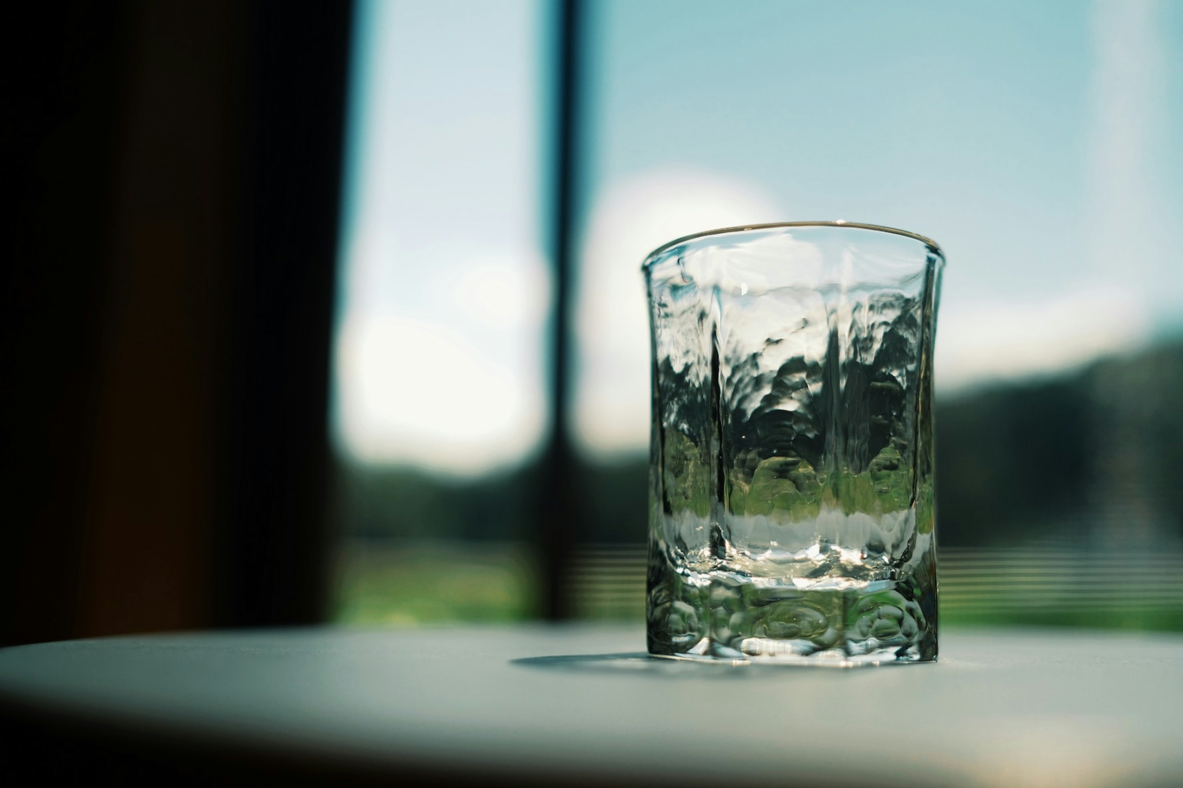 A clear glass sitting on a table with a view of the outdoors in the background