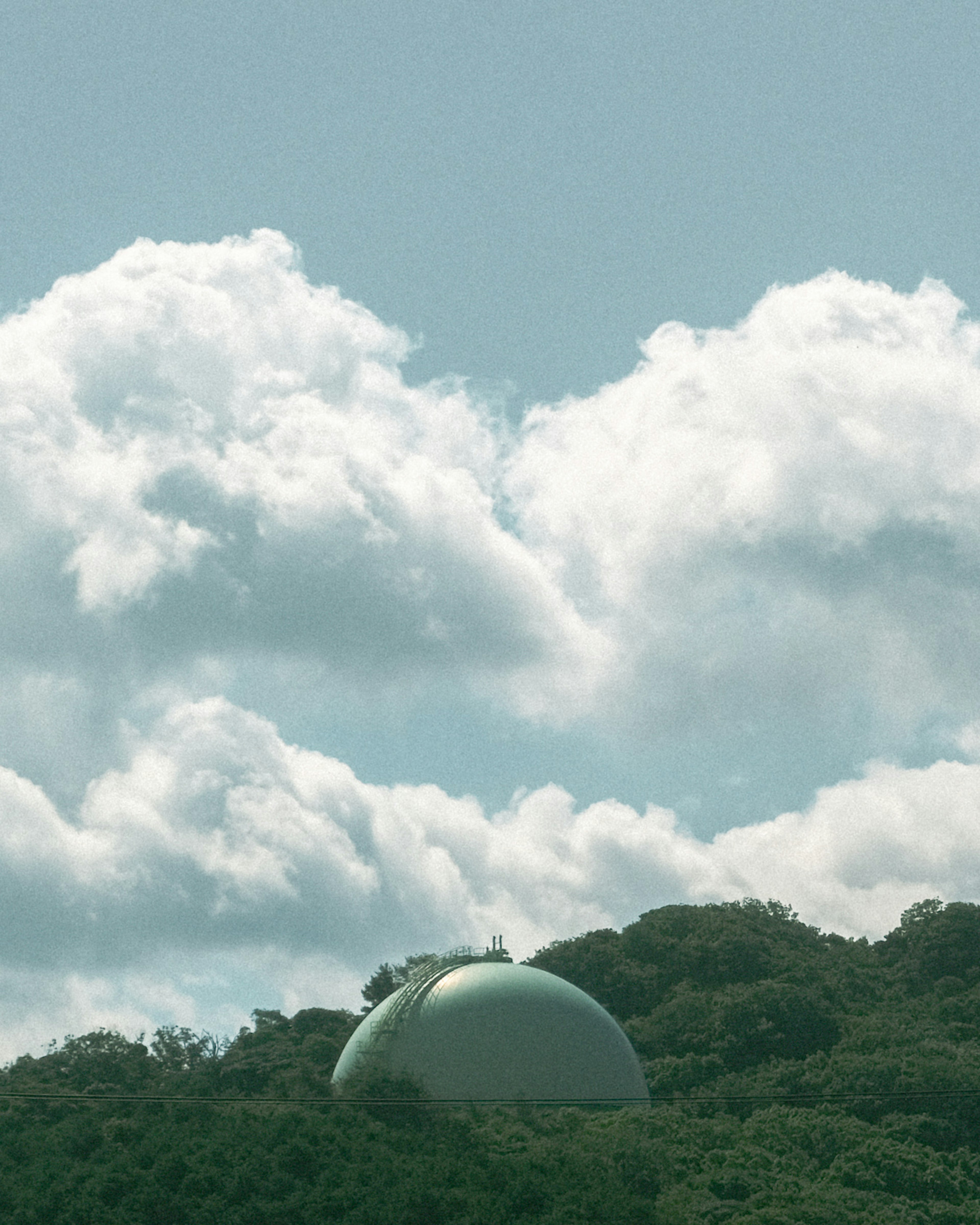 Structure en forme de dôme sur une colline verte sous un ciel bleu avec des nuages blancs duveteux