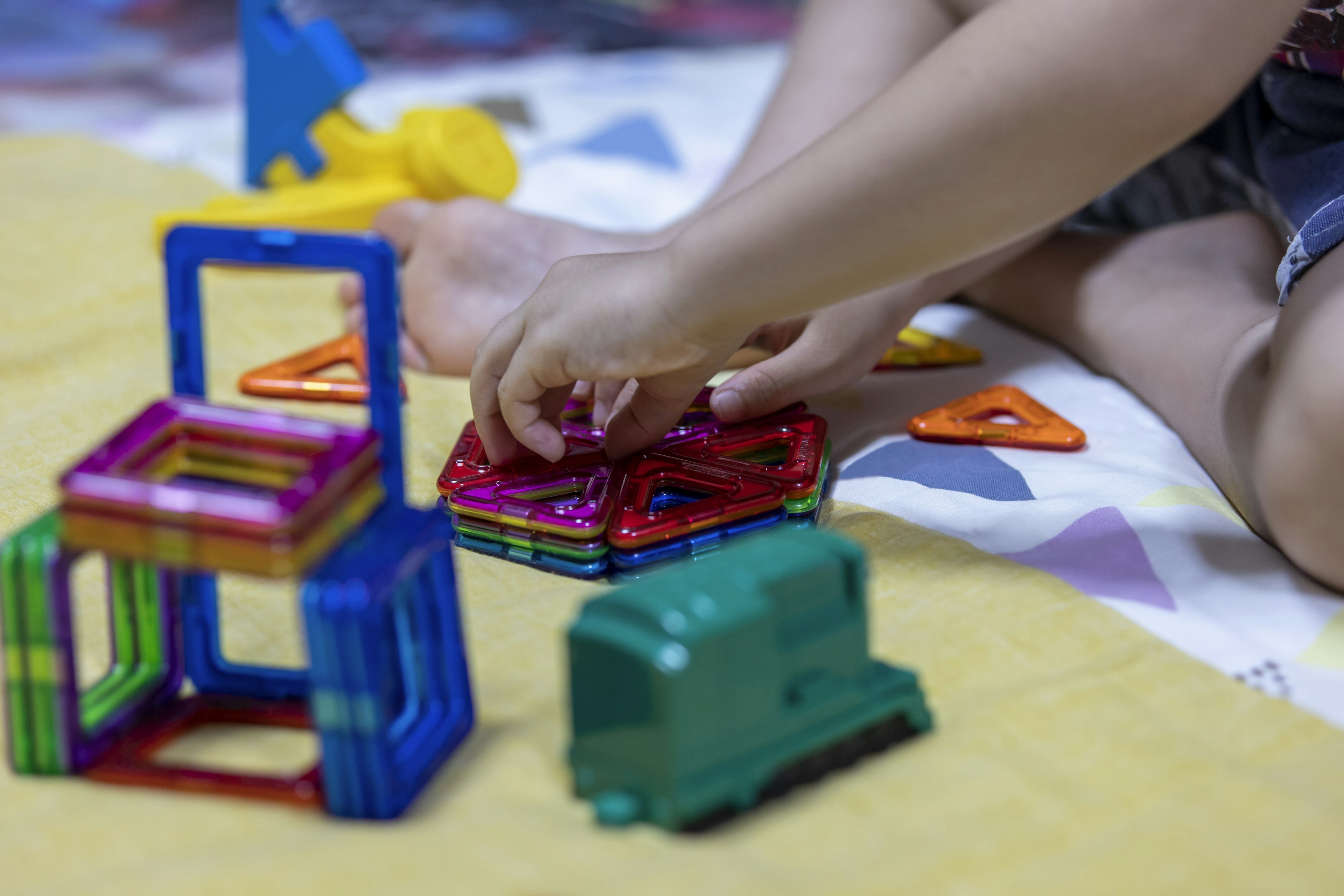 Kind spielt mit bunten Bausteinen mit verschiedenen Formen und einem grünen Spielzeugtruck