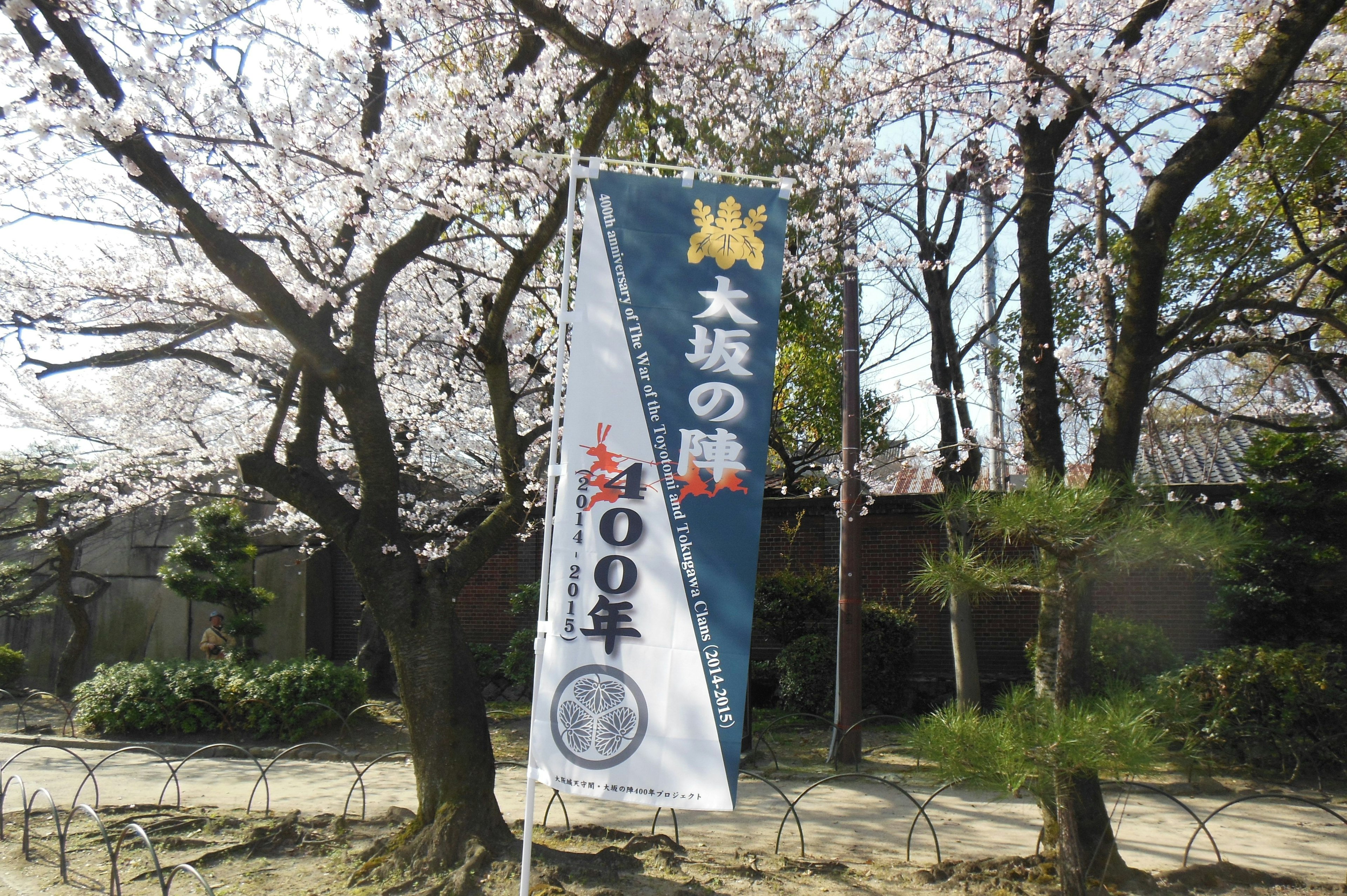 ธงสีน้ำเงินใต้ต้นซากุระที่มีข้อความ Dazaifu และวันครบรอบ 100 ปี