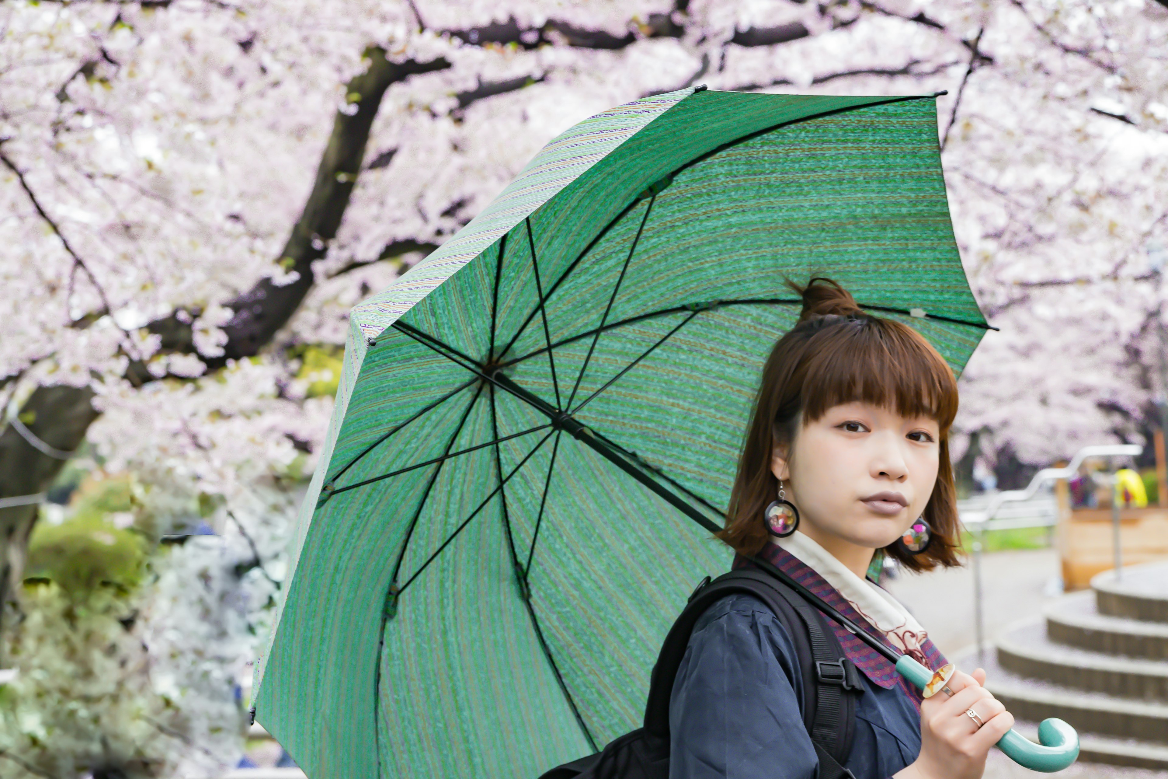 Femme tenant un parapluie vert sous des cerisiers en fleurs