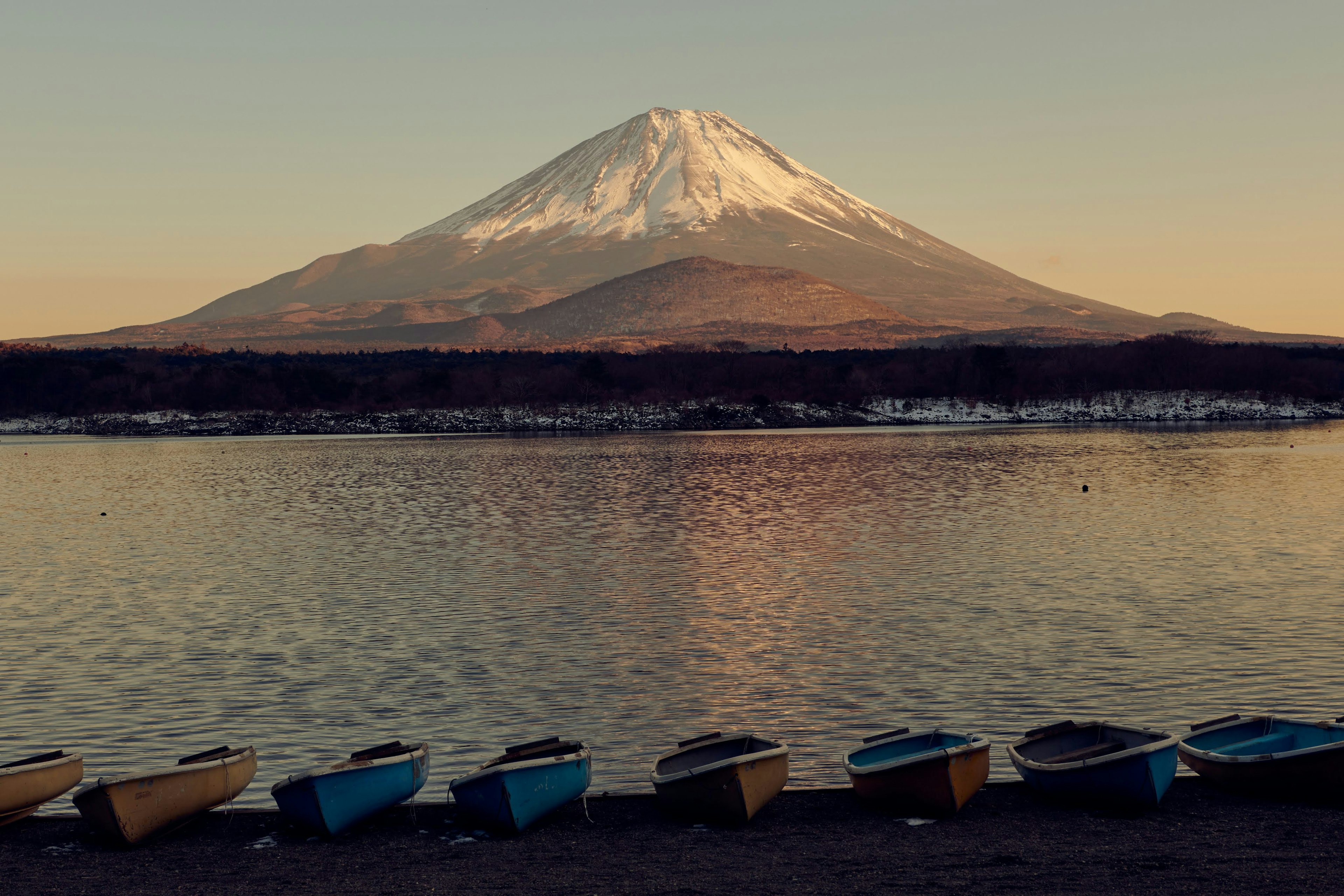 Der Fuji erhebt sich über einen ruhigen See bei Sonnenuntergang mit bunten Booten im Vordergrund