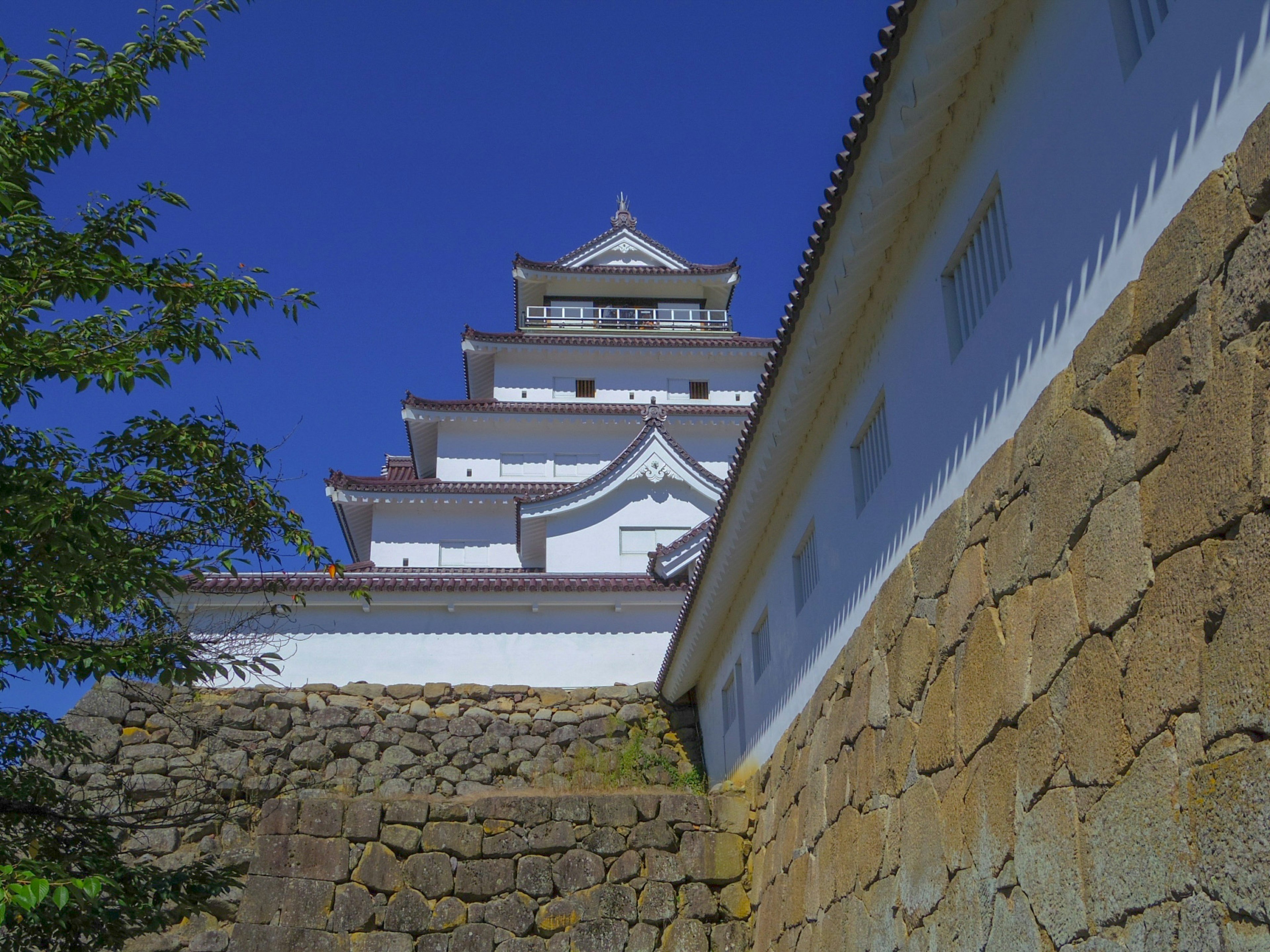 Blick auf ein Schloss mit weißen Wänden und steinerner Grundlage vor blauem Himmel